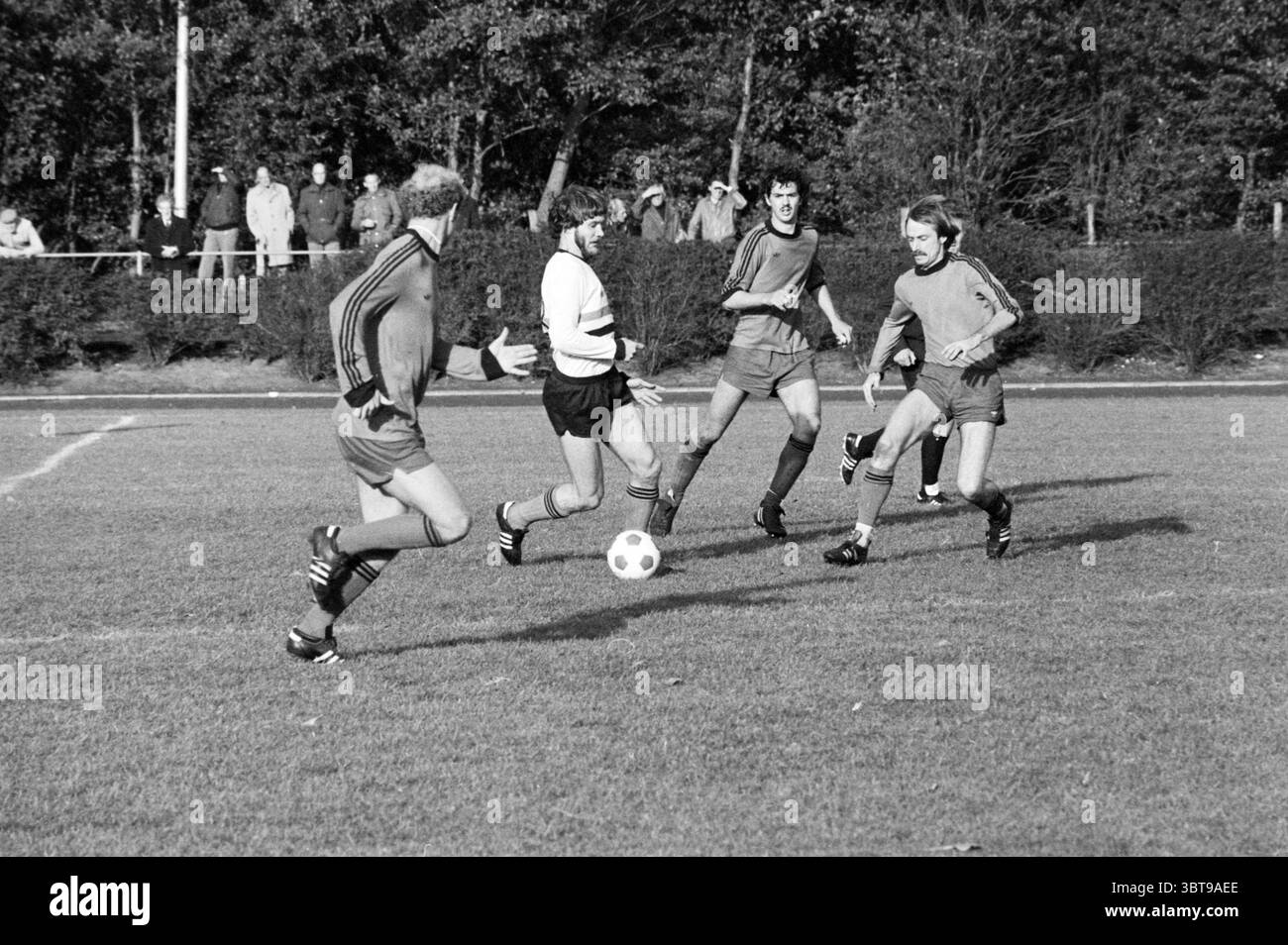Lisse Boys - Jodan Boys Football, Whizgle News, Dutch Desk, Paesi Bassi, 1950 - 2000 il 18-10-1980. Questi sono gli elementi dell'immagine. La scena cattura un momento intenso durante una partita di calcio. In primo piano, un giocatore con una maglia bianca sta manovrando abilmente la palla, circondato dagli avversari con abiti colorati a contrasto, uno in una maglia blu e due in tonalità più scure. I loro corpi sono disposti in posizioni dinamiche, mostrando atletismo e concentrazione, mentre si impegnano nel gioco. Il campo è un verde vivace, ben tenuto e punteggiato di macchie di terra dove l'erba è stata bagnata Foto Stock
