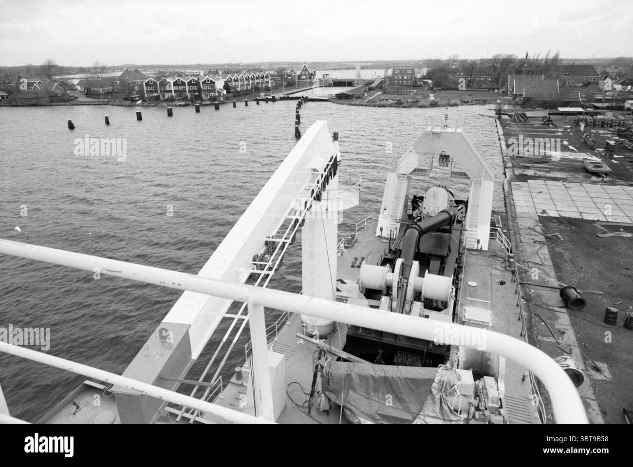 Panoramica del cantiere navale Stapel Spaarndam Shipping Spaarndam, Whizgle News, Dutch Desk, Paesi Bassi, 1950 - 2000 il 18-12-1986. L'immagine contiene questi argomenti. La scena cattura un ambiente marittimo, in cui una grande nave è ancorata lungo un corpo d'acqua. La vista e' presa da un alto punto panoramico, che offre un'ampia prospettiva dei dintorni. In primo piano, il ponte della nave è visibile, mostrando vari macchinari e strutture tipiche delle operazioni marittime. Diversi grandi verricelli e cavi industriali sono posizionati in modo prominente, a indicare lo scopo funzionale della nave. TH Foto Stock