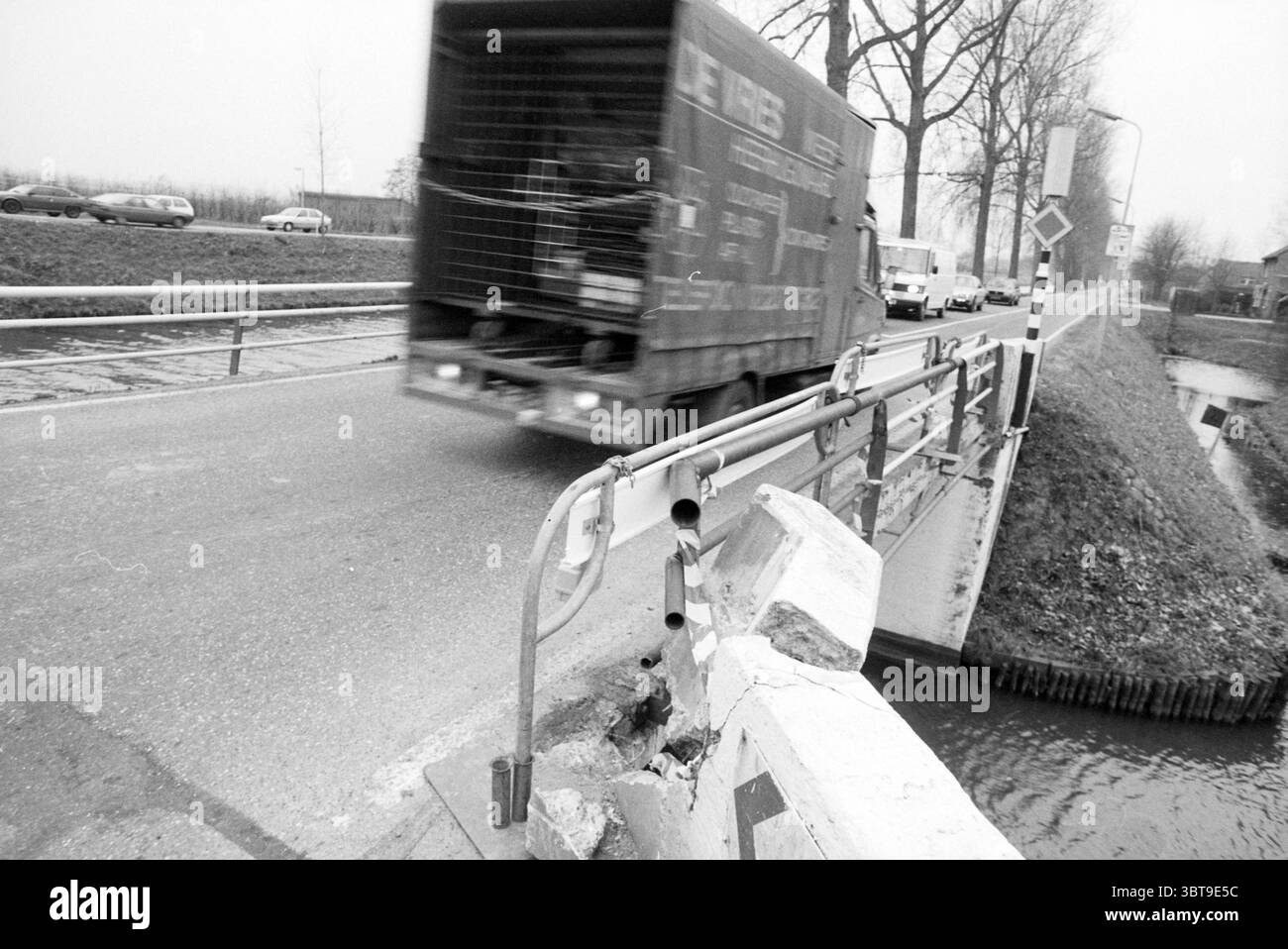 Bridge ha colpito Vijfhuizerweg Vijfhuizerweg, Whizgle News, Dutch Desk, Paesi Bassi, 1950 - 2000 il 09-12-1990. L'immagine mostra questi argomenti. La scena cattura un momento dinamico su strada con un senso di movimento e urgenza. Un grande autocarro, parzialmente oscurato dalla velocità, domina un lato del telaio, con i suoi esterni dipinti in toni tenui che si fondono con il cielo coperto. Il carrello sembra passare sopra un ponte stretto, delimitato da una semplice barriera di protezione metallica, che mostra segni di usura e danni, in particolare in un punto in cui è scheggiato e sbriciolato. Lo sfondo presenta un collettio Foto Stock