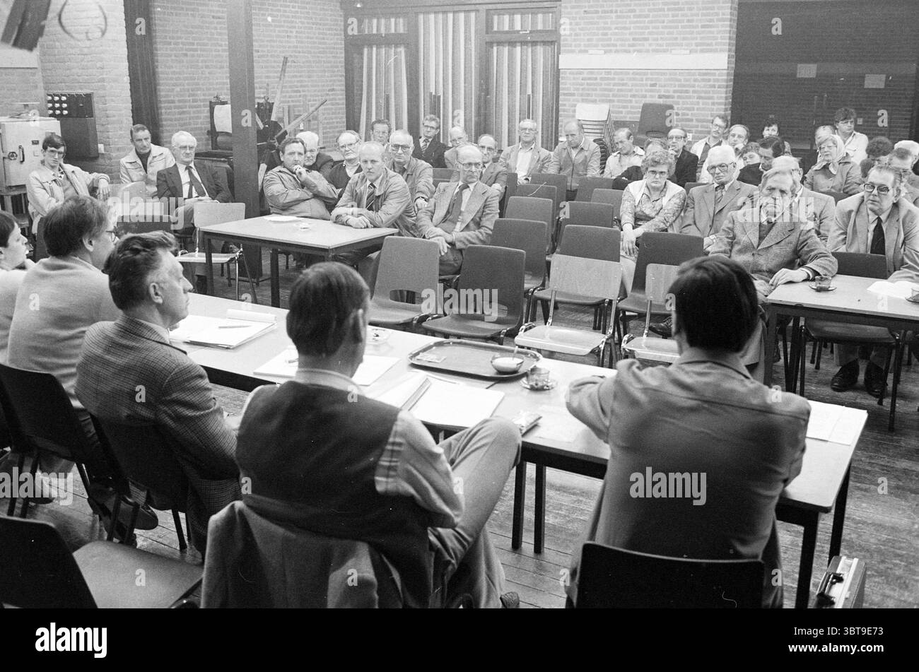 Abbonati TV via cavo Meeting Beverwijk Meetings Beverwijk Paesi Bassi, Whizgle News, Dutch Desk, Paesi Bassi, 1950 - 2000 il 18-05-1983. Questi sono gli argomenti nell'immagine. La scena raffigura un raduno in una sala spaziosa e ben illuminata con un soffitto alto. Le pareti sono costruite con mattoni rossi a vista, donando un'atmosfera calda ma industriale all'ambiente. I tavoli disposti in forma rettangolare dominano il primo piano, con diversi individui seduti intorno a loro. I partecipanti ai tavoli sono un mix di uomini più anziani, ognuno vestito in abiti formali tipici della metà del XX secolo. Molti wea Foto Stock