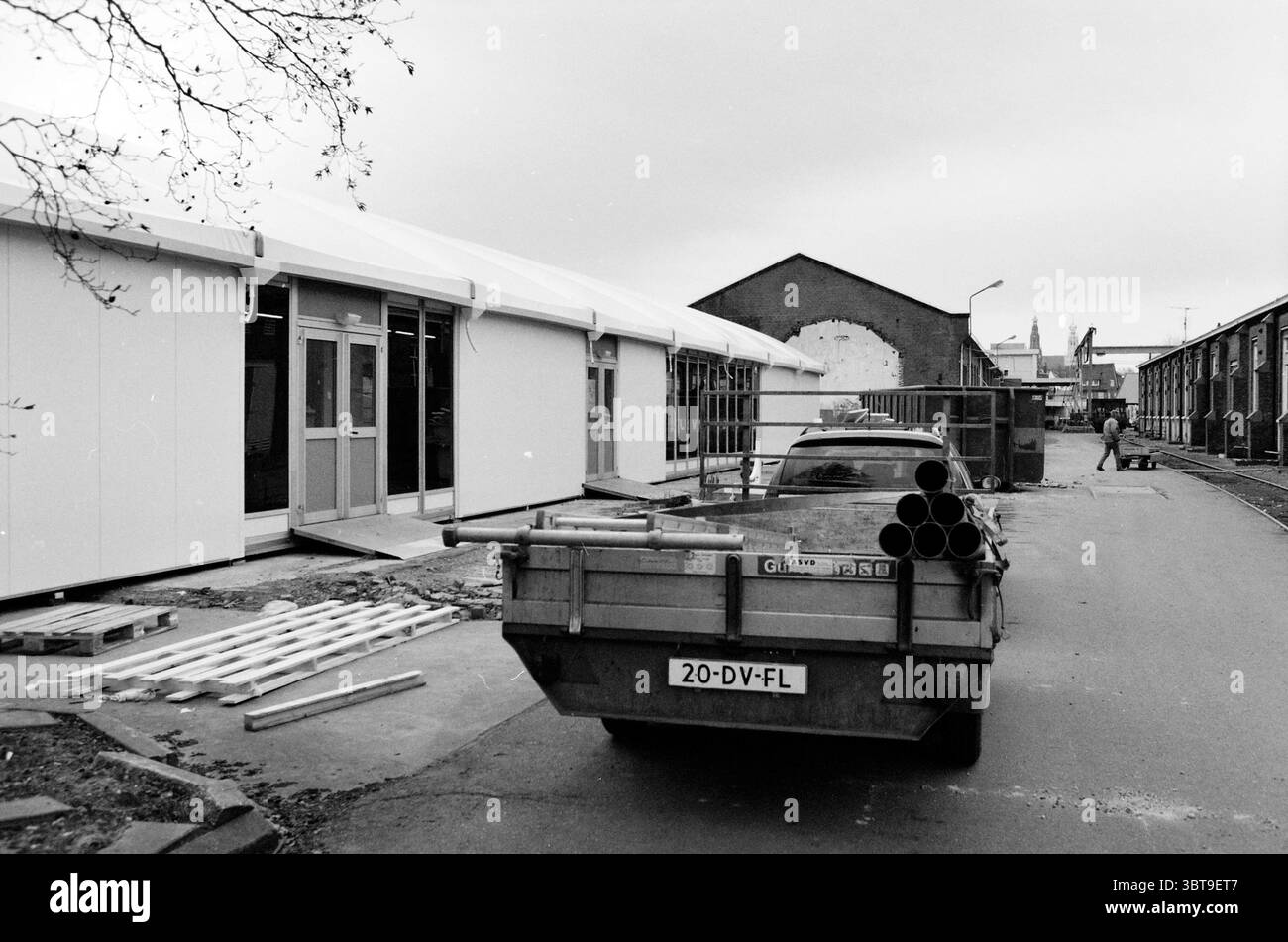 Costruzione di una mensa temporanea per Nedtrain Haarlem Paesi Bassi, Whizgle News, Dutch Desk, Paesi Bassi, 1950 - 2000 il 14-01-2003. Questi sono gli elementi dell'immagine. La scena raffigura un'area di costruzione caratterizzata da una tavolozza monocromatica, che suggerisce un giorno nuvoloso o coperto che proietta una luce soffusa in tutto l'ambiente. Sulla sinistra, una struttura temporanea con un esterno bianco è ben visibile, con le sue grandi porte di vetro che riflettono un cielo grigio tenue. L'edificio appare funzionale e nuovo, in contrasto con l'ambiente circostante. In primo piano, un veicolo di servizio Foto Stock