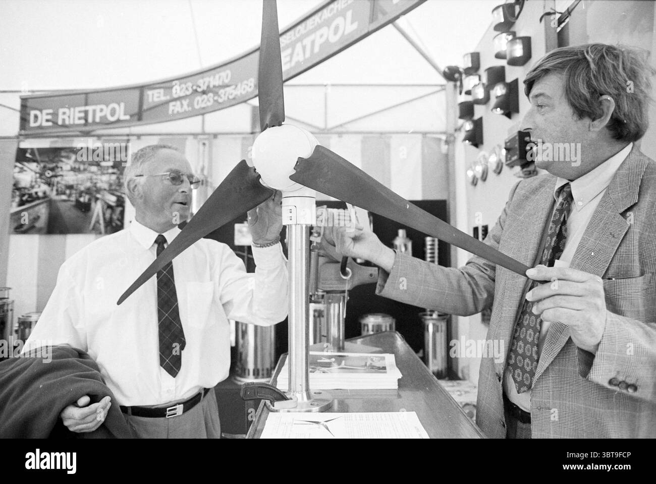 Stand del cantiere navale di Rietpol alla mostra Hiswa Amsterdam Paesi Bassi, Whizgle News, Dutch Desk, Paesi Bassi, 1950 - 2000 il 07-09-1995. Questi sono gli argomenti nell'immagine. In un ambiente espositivo vivace, due uomini sono impegnati in una conversazione con entusiasmo visibile. Un individuo che indossa occhiali e una camicia bianca con cravatta scura esamina da vicino un modello di piccola turbina eolica. Le lame del modello sono nere, in contrasto con una sfera bianca brillante al centro, suggerendo una particolare attenzione alla tecnologia o all'energia rinnovabile. L'uomo che interagisce con lui è vestito casualmente di un gr Foto Stock