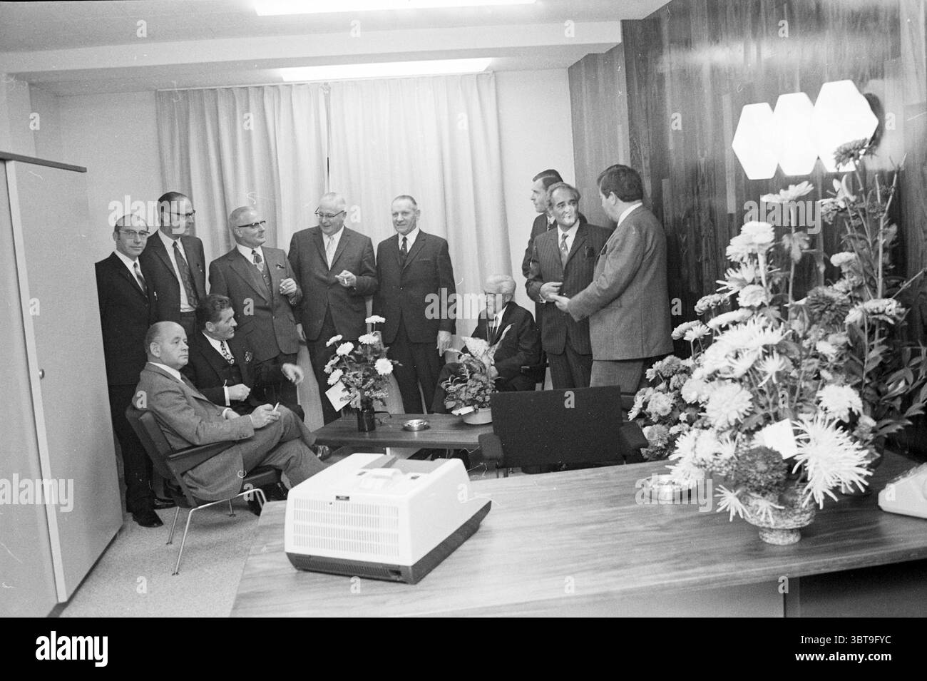 Foto di gruppo del Consiglio di amministrazione della Housing Association Haarlem. Groups, Whizgle News, Dutch Desk, Paesi Bassi, 1950 - 2000 on 30-10-1971. L'immagine mostra questi argomenti. La scena presenta un incontro di un gruppo di uomini ben vestiti, la maggior parte dei quali indossa abiti e cravatte. Sono collocate in una camera moderna e minimalista caratterizzata da una combinazione di toni neutri e caldi accenti di legno. Una grande tenda da pavimento a soffitto sullo sfondo diffonde delicatamente la luce proveniente dall'alto, che aggiunge un'illuminazione luminosa ma delicata all'ambiente. In primo piano sono seduti alcuni individui, uno dei quali Foto Stock