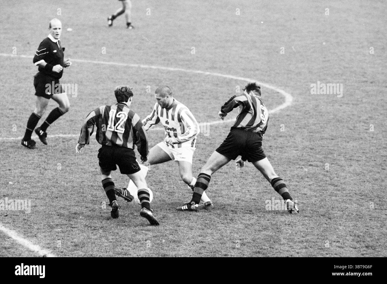 Football EDO - Aalsmeer, Whizgle News, Dutch Desk, Paesi Bassi, 1950 - 2000 il 19-11-1994. Questi argomenti vengono visualizzati nell'immagine. La scena cattura un momento dinamico su un campo da calcio, dando vita all'energia e alla tensione di una partita competitiva. In primo piano, tre giocatori sono impegnati in uno scambio acceso. Un giocatore, vestito con un'impressionante divisa bianca con strisce orizzontali, sembra essere al centro dell'attenzione, manovrando abilmente la palla mentre affronta due avversari. Il loro linguaggio del corpo suggerisce concentrazione e determinazione, con muscoli tesi e occhi fissi sul bersaglio. L'opposto Foto Stock