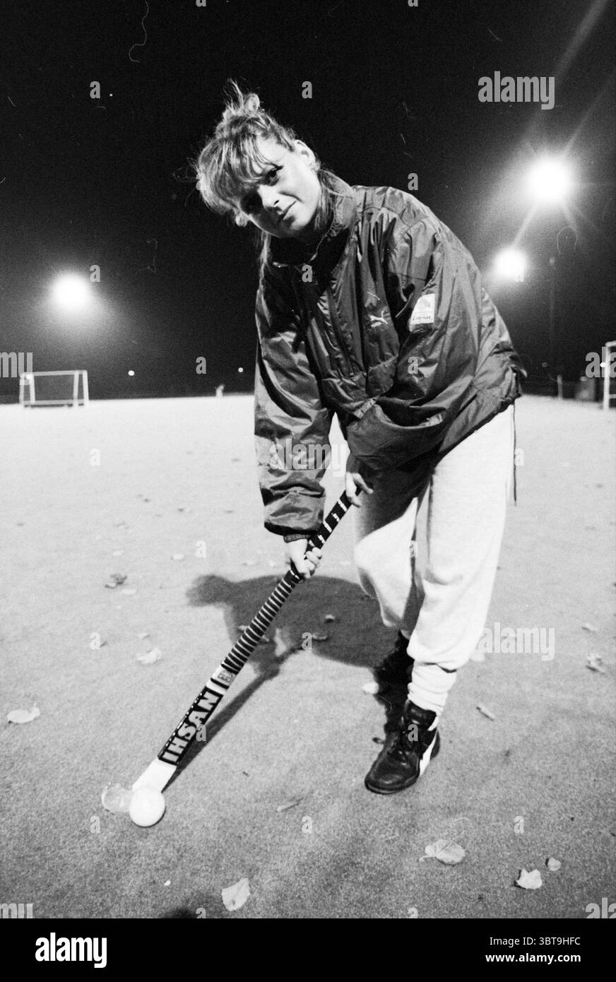 Ingrid Deenen hockey B'daal Hockey Bloemendaal, Whizgle News, Dutch Desk, Paesi Bassi, 1950 - 2000 il 25-10-1989. Questi sono gli elementi dell'immagine. In un ambiente esterno scarsamente illuminato, una giovane donna sta in piedi con un bastone da hockey in mano. Indossa una giacca oversize e ingombrante, comoda e casual, con le maniche leggermente rivolte verso l'alto per rivelare un comodo outfit atletico. I suoi pantaloni antisudore sono appesi in modo allentato, aggiungendo un tocco di relax alla scena. I suoi capelli sono legati liberamente, alcuni fili cadono dolcemente intorno al suo viso, dandole un aspetto vivace. Il ligh Foto Stock