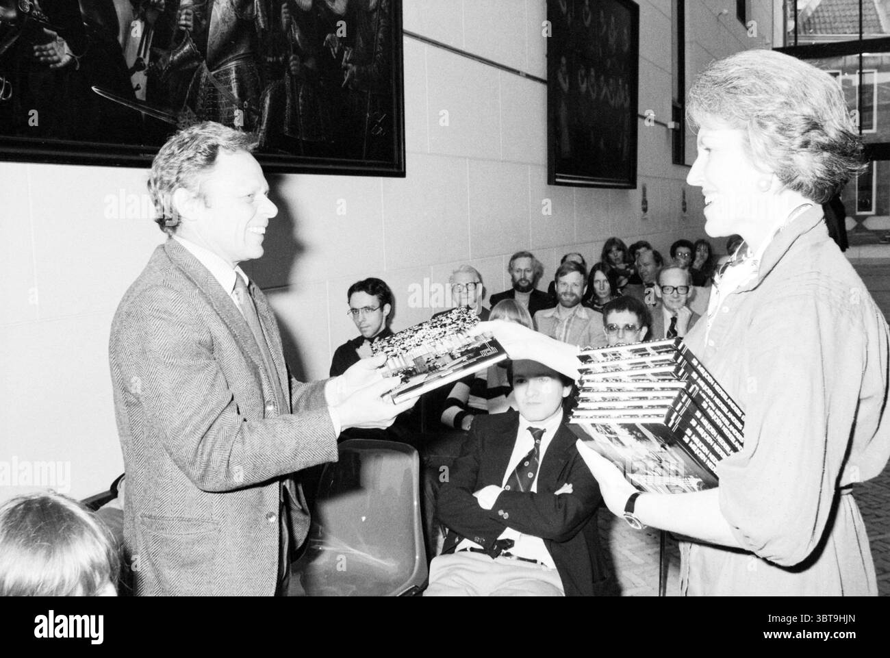 Libro di presentazione 58 milioni di olandesi e le loro chiese Amsterdam Spectrum Amsterdam Paesi Bassi, Whizgle News, Dutch Desk, Paesi Bassi, 1950 - 2000 il 06-04-1979. L'immagine include questi argomenti. In un vivace ambiente interno, due persone sono prominentemente impegnate in un momento di interazione. Uno sembra essere un uomo, vestito con un abito classico con una camicia di colore chiaro. La sua espressione è calda e aperta, suggerendo un comportamento amichevole mentre estende le mani verso una donna di fronte a lui. La donna, vestita elegantemente, ha una pila di libri ben legati, che aggiunge uno strato di segno Foto Stock