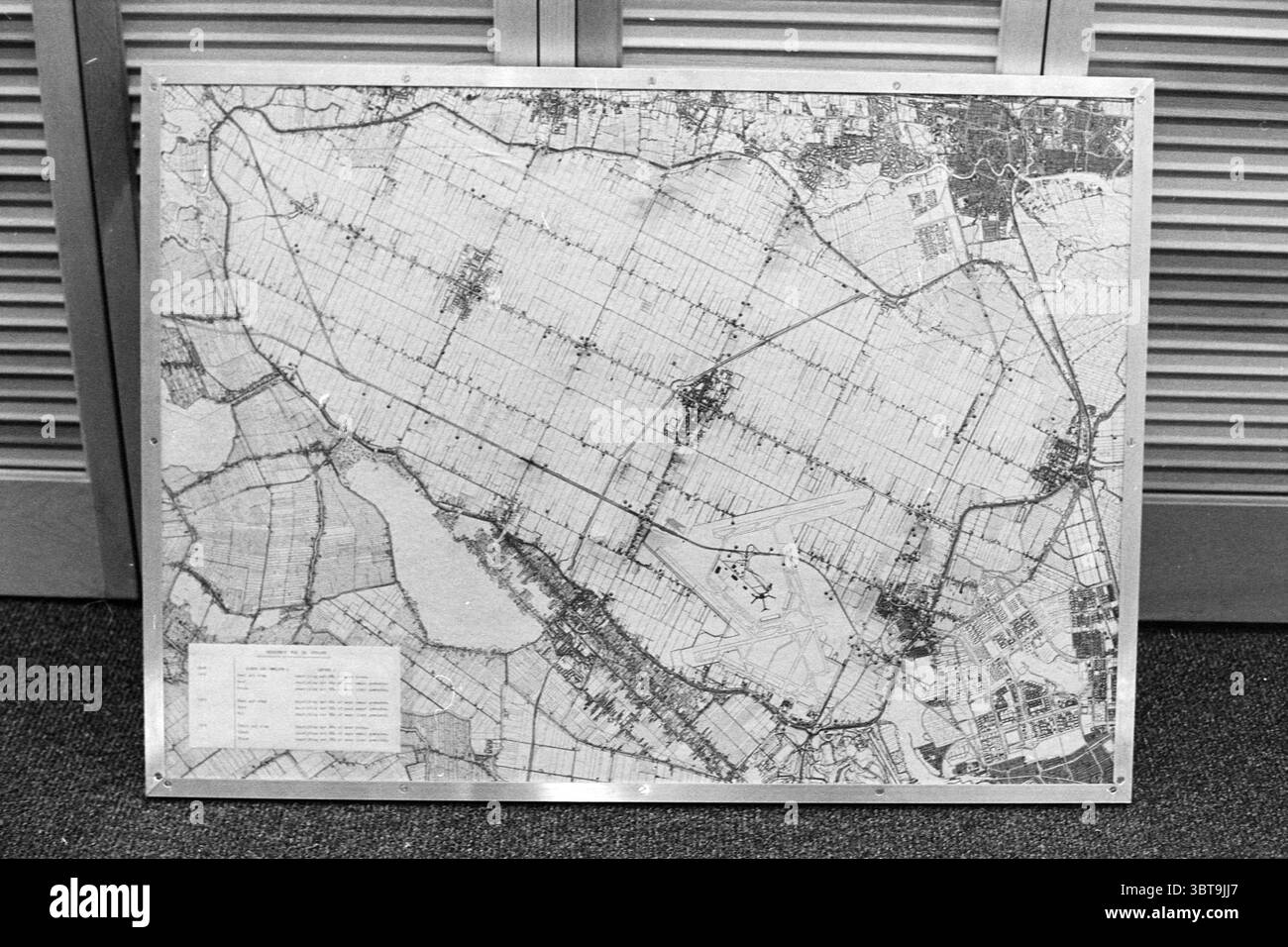 Mappa di Schiphol e della zona di Haarlemmermeer, Whizgle News, Dutch Desk, Paesi Bassi, 1950 - 2000. L'immagine include questi argomenti. In un ambiente ben illuminato, una mappa grande e dettagliata viene visualizzata in modo prominente su una superficie piana, attirando l'attenzione con il suo design intricato. La mappa presenta una rete di linee, che probabilmente rappresentano strade o sentieri, attraversano sezioni contrassegnate da varie sfumature di colori chiari e scuri. In primo piano, diverse aree sono densamente raggruppate, suggerendo ambienti urbani o punti di riferimento significativi. Ogni sezione della mappa contrasta con le altre, creando un Foto Stock