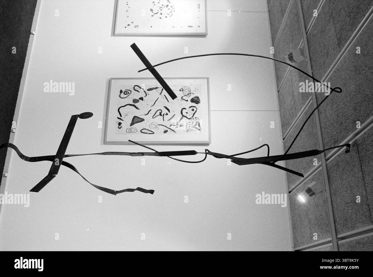 Opere d'arte di Jack Prins IJm. Haarlem Paesi Bassi, Whizgle News, Dutch Desk, Paesi Bassi, 1950 - 2000 il 03-09-1996. Questi sono gli elementi dell'immagine. La scena presenta una mostra d'arte contemporanea all'interno di una galleria. A sinistra, una grande scultura astratta realizzata con curve in metallo scuro e piegata in varie direzioni, creando linee dinamiche che attirano l'attenzione. La superficie della scultura ha una finitura opaca, che ne esalta l'estetica moderna e contrasta con l'ambiente più leggero. Sullo sfondo, un'opera d'arte incorniciata è appesa al muro, composta da sporadici segni di inchiostro nero Foto Stock