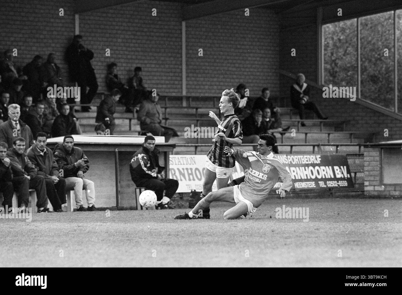 Football RCH - Ripperda, Whizgle News, Dutch Desk, Paesi Bassi, 1950 - 2000 il 11-11-1995. L'immagine contiene questi argomenti. La scena cattura un momento intenso su un campo da calcio. In primo piano, due giocatori sono impegnati in un gioco chiave; uno, vestito con strisce nere e rosse, sta manovrando con abilità la palla, mentre l'altro, rivestito con una maglia blu vivace, sta tentando un placcaggio scorrevole da dietro, creando un senso di urgenza. Le tribune dello stadio sono popolate da spettatori, le loro espressioni vanno dall'anticipazione alla preoccupazione, contribuendo a creare un'atmosfera elettrica. La folla lo è Foto Stock