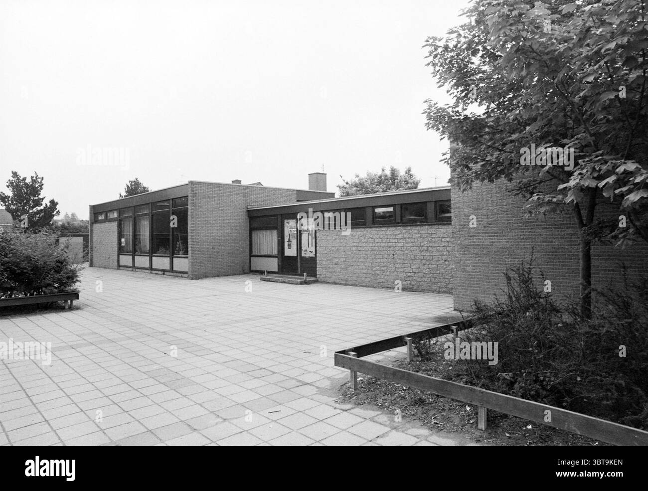 Esterno De Otterkolken Heemskerk Schools Heemskerk, Whizgle News, Dutch Desk, Paesi Bassi, 1950 - 2000 il 16-06-1982. Questi sono gli elementi dell'immagine. La scena raffigura una struttura architettonica moderna caratterizzata da linee pulite e design funzionale. L'edificio è costruito principalmente in mattoni, mostrando una miscela di texture e sfumature di grigio, creando un'estetica silenziosa e minimalista. La facciata presenta grandi finestre che permettono alla luce naturale di inondare gli interni, riflettendo un senso di apertura e connessione con l'esterno. Intorno all'edificio, il terreno è pavimentato Foto Stock