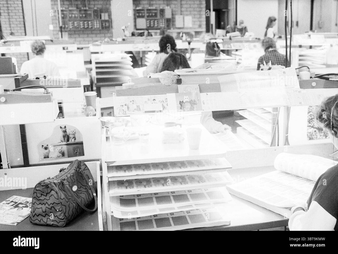Società di stampa varie Enschedéen Zn. Enschede & Zn industria grafica MV Joh. Haarlem Paesi Bassi, Whizgle News, Dutch Desk, Paesi Bassi, 1950 - 2000 il 26-04-1988. Questi argomenti sono mostrati nell'immagine. La scena cattura uno spazio di lavoro occupato con diverse persone impegnate in varie attività. L'ambiente sembra essere un grande studio o un ufficio ben illuminato, caratterizzato da lunghe file di tavoli carichi di fogli e materiali che suggeriscono un'attenzione particolare al layout o al lavoro di progettazione. I colori sono prevalentemente attenuati, con una tavolozza monocromatica che crea un senso di nostalgia e che enfatizza il travaglio inte Foto Stock