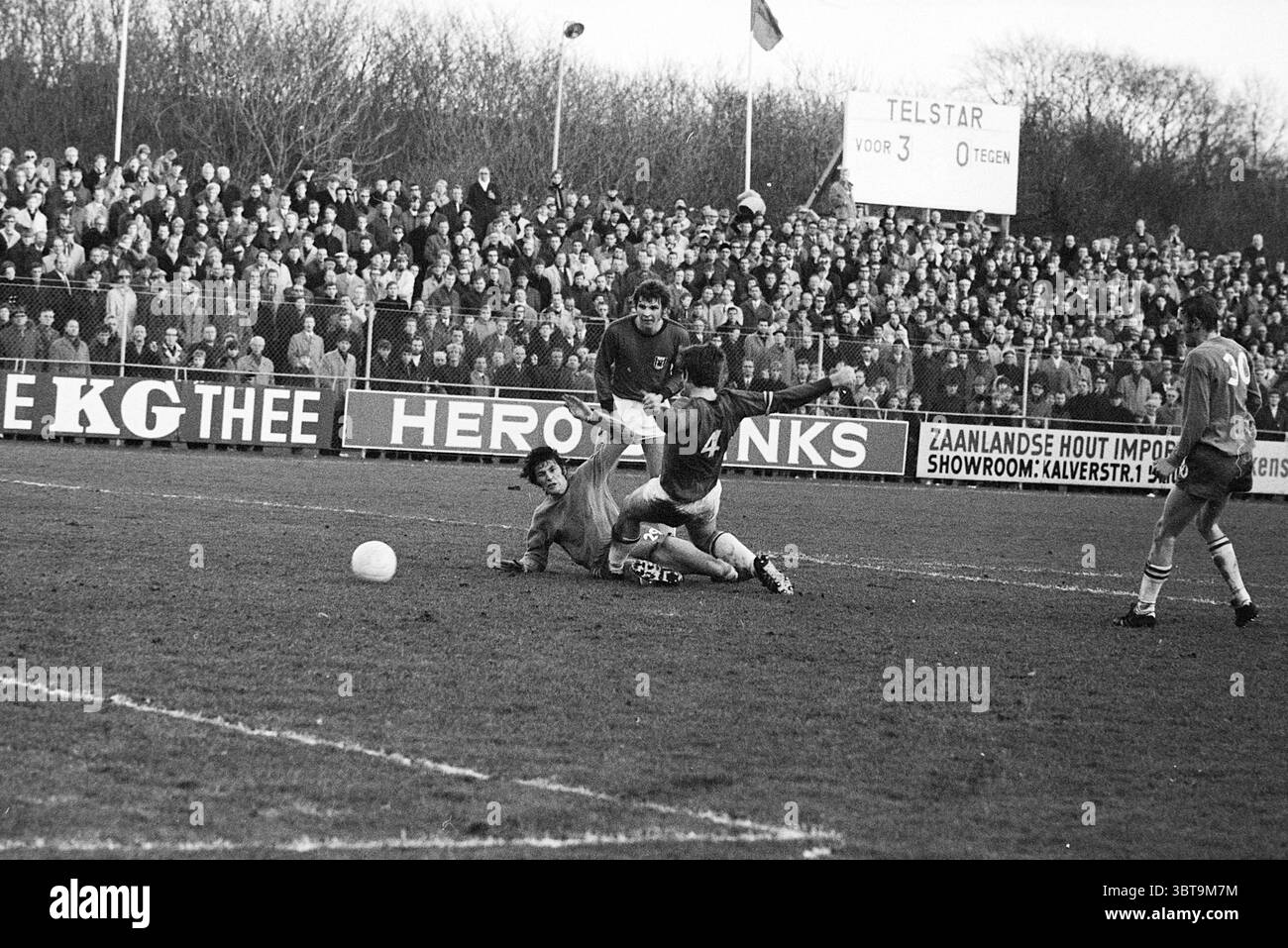 Telstar - AZ'67 Football Telstar, Whizgle News, Dutch Desk, Paesi Bassi, 1950 - 2000 il 20-12-1970. Questi argomenti sono mostrati nell'immagine. La scena cattura un momento intenso in una partita di calcio, in cui due giocatori sono impegnati in una lotta per il possesso della palla. Un giocatore, vestito con una maglia scura, è a terra, presumibilmente tentando di riprendere il controllo dopo una collisione, mentre l'altro, indossando una maglia numerata, è in una posa dinamica, probabilmente cercando di sfidare la palla. Lo sfondo è pieno di una folla di spettatori, vestiti con abiti invernali, che suggeriscono un'atmosfera fredda. Foto Stock