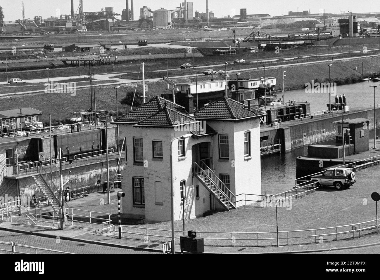 Esterno Sluisplein 3 IJmuiden IJmuiden Sluisplein Paesi Bassi, Whizgle News, Dutch Desk, Paesi Bassi, 1950 - 2000 il 16-07-1996. Questi argomenti vengono visualizzati nell'immagine. La scena presenta una tranquilla area fronte mare, caratterizzata da una prominente struttura a due piani con un distintivo tetto triangolare adornato con piastrelle. Questo edificio, dipinto in una tonalità chiara, si distingue sullo sfondo industriale circostante. La sua architettura presenta un design pratico, caratterizzato da grandi finestre e una scala che porta ad un livello superiore, offrendo una vista sul canale. Intorno alla struttura, il Foto Stock