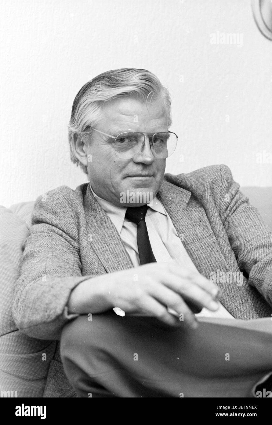 Ritratto di un uomo, Whizgle News, Dutch Desk, Paesi Bassi, 1950 - 2000. L'immagine mostra questi argomenti. Un uomo è seduto comodamente su un divano di colore chiaro, trasuda un comportamento rilassato ma attento. I suoi capelli argentati, leggermente arruolati, contrastano con la cravatta scura, che è ben annodata. Indossa un blazer ben aderente che aggiunge un tocco di raffinatezza. I suoi occhiali, con montature sottili, mettono in risalto il suo sguardo concentrato. Lo sfondo è un tono morbido e silenzioso, che sottolinea il soggetto senza distogliere l'attenzione da lui. L'illuminazione generale e' calda e delicata, creando un'atmosfera intima che migliora Foto Stock