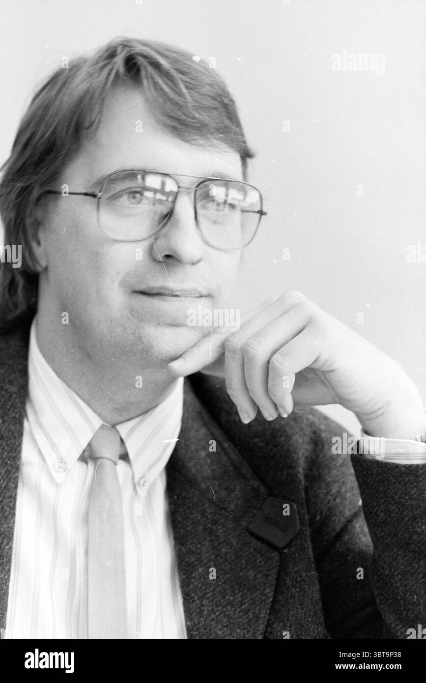 Rob Meerhof Patient Organization, Whizgle News, Dutch Desk, Paesi Bassi, 1950 - 2000 il 12-02-1991. L'immagine mostra questi argomenti. La scena vede un uomo con un'espressione premurosa, seduto a un tavolo. I suoi capelli sono marrone chiaro e leggermente ruvidi. Indossa grandi occhiali rotondi che accentuano il suo sguardo, trasmettendo un'aria di contemplazione. L'uomo è vestito con un abbigliamento formale, composto da un blazer scuro su una camicia di colore chiaro a righe sottili, abbinato a una cravatta che completa il look generale. Lo sfondo è leggermente sfocato, sottolineando il soggetto senza attirare l'attenzione Foto Stock