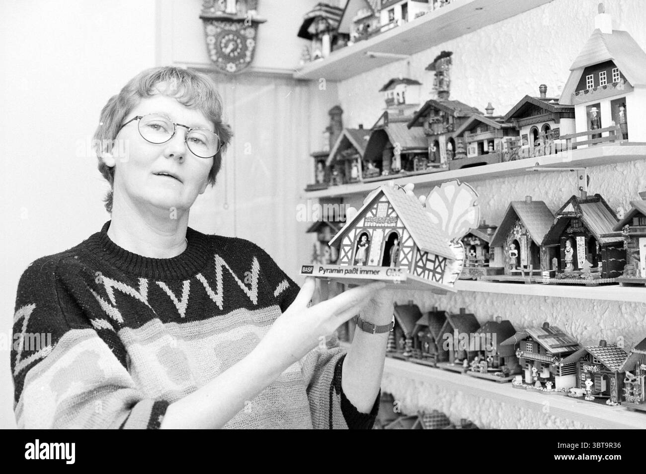 Mrs. Wittekoek Weather Houses, Whizgle News, Dutch Desk, Paesi Bassi, 1950 - 2000 il 13-12-1993. Questi sono gli elementi dell'immagine. In un ambiente interno accogliente, una donna si erge con fiducia, mostrando una piccola casa in miniatura dal design complesso. Ha capelli corti e chiari e indossa occhiali rotondi che si appoggiano leggermente sul naso. Il suo maglione è lavorato a maglia con un'ampia fantasia a righe, caratterizzata da tonalità naturali come marroni e creme, che evocano un senso di calore e comfort. Intorno a lei, una collezione di case in miniatura adorna le pareti, ordinatamente disposte su diversi scaffali. Queste case variano nell'arco Foto Stock