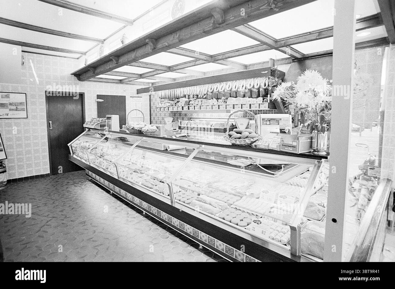 INTR. Butcher van 't Hoff en Zonen Interior, Whizgle News, Dutch Desk, Paesi Bassi, 1950 - 2000 il 01-10-1974. L'immagine include questi argomenti. La scena presenta un caratteristico spazio interno, probabilmente un panificio o una gastronomia, caratterizzato da un'atmosfera nostalgica e invitante. Il punto focale è una lunga vetrina, piena di una serie di torte, pasticcini e altri prodotti da forno, ognuna splendidamente disposta per mostrare i loro colori e le loro texture seducenti. La cassa in vetro riflette una delicata lucentezza, esaltando il fascino visivo delle prelibatezze all'interno, che vanno dai dolci dorati a quelli vivaci, Foto Stock
