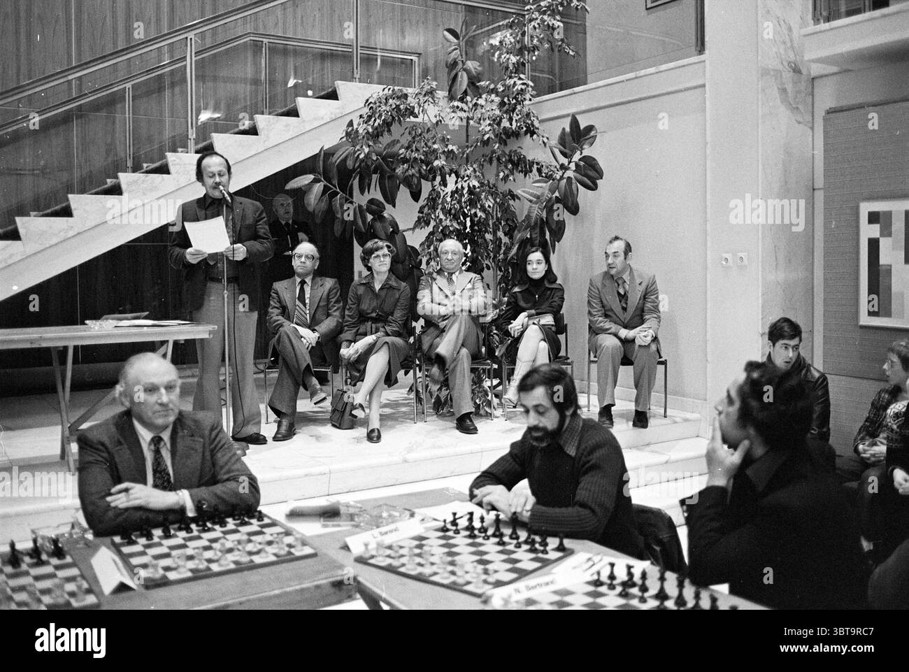 Finale + cerimonia di premiazione Wijk aan Zee Blast Furnace Chess Tournament cerimonia di premiazione, Whizgle News, Dutch Desk, Paesi Bassi, 1950 - 2000 il 27-01-1978. Questi sono gli argomenti nell'immagine. La scena si sviluppa in un ambiente interno caratterizzato da un mix di architettura moderna e un'atmosfera serena. Una scala, elegantemente progettata con una combinazione di linee eleganti e superfici lisce, sale dal primo piano, che conduce ad una spaziosa area sopra. Lo spazio è ben illuminato, evidenziando le superfici lucide e proiettando ombre delicate. Al centro, un gruppo di persone è impegnato in un che Foto Stock