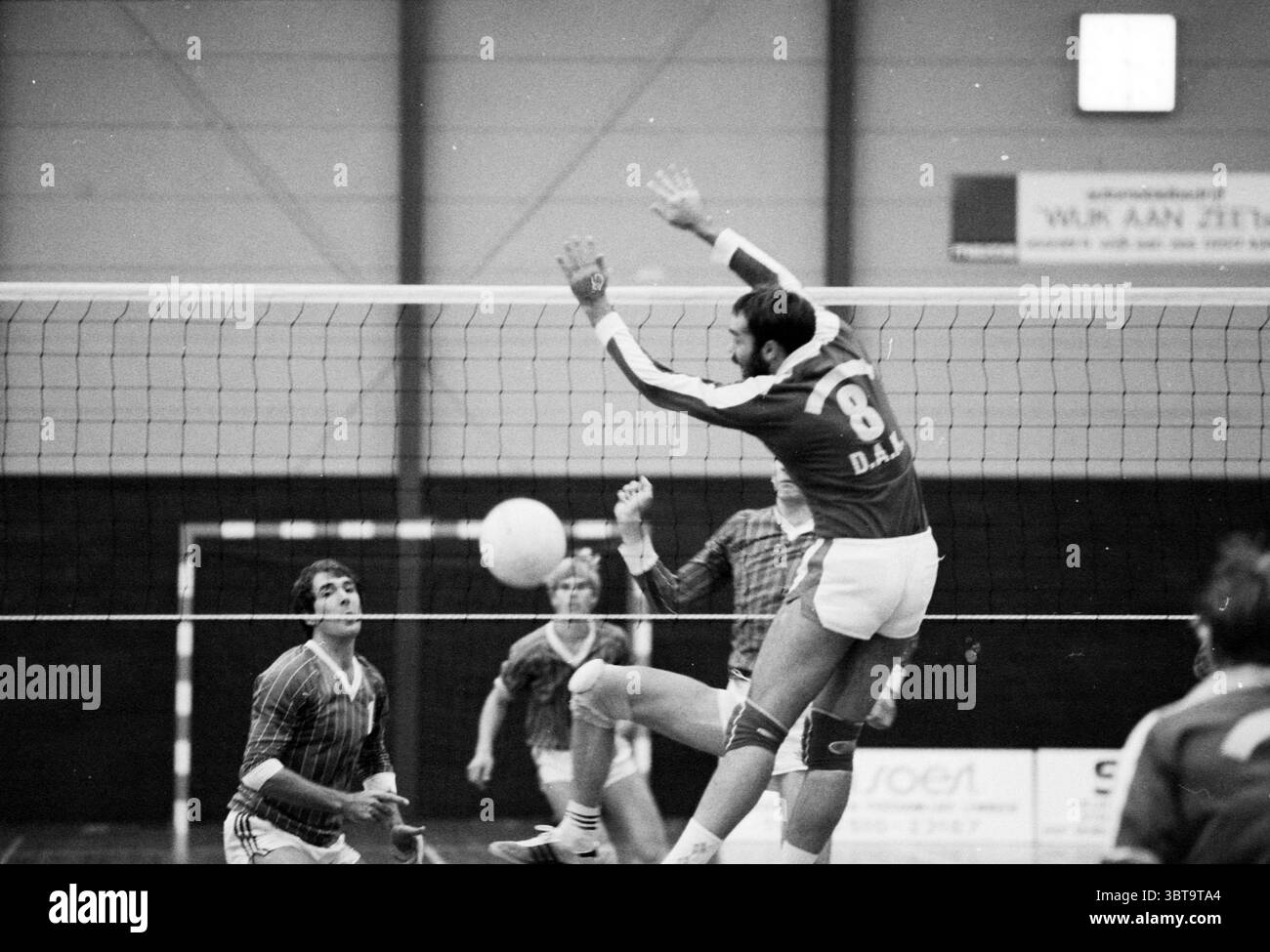 WVV - DAK Volleyball, Whizgle News, Dutch Desk, Paesi Bassi, 1950 - 2000 il 27-10-1985. L'immagine include questi argomenti. La scena cattura un momento dinamico di una partita di pallavolo in interni. Al centro della composizione c'è un giocatore, pronto a mezz'aria, con una forte attenzione alla sua forma atletica mentre fa un salto impressionante. Indossa una maglia scura, nota per il suo numero audace sul retro, che contrasta con gli shorts più leggeri. Sullo sfondo, sono posizionati diversi compagni di squadra e avversari, ciascuno con livelli diversi di concentrazione e prontezza. Viene visualizzato un giocatore leggermente sfocato Foto Stock