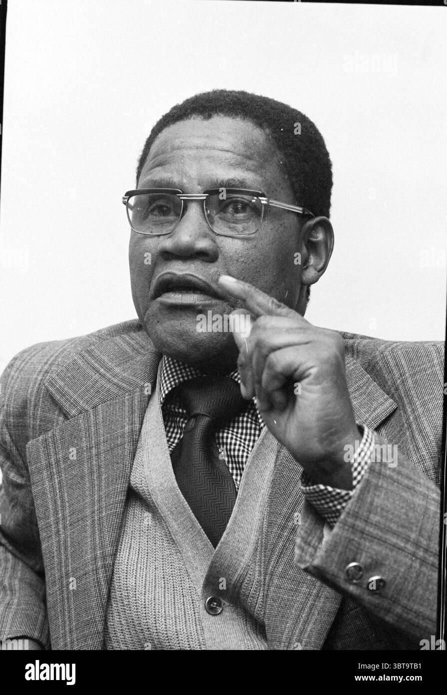 SACTU leader sindacato sudafricano {South Africa Congress of Trade Unions) persone sindacati, Whizgle News, Dutch Desk, Paesi Bassi, 1950 - 2000 il 01-11-1978. Questi argomenti vengono visualizzati nell'immagine. La scena presenta un individuo seduto, trasuda un senso di autorità e contemplazione. È vestito con un abito grigio sartoriale con un gilet ben aderente, che incarna un aspetto formale e raffinato. Il motivo intricato della sua cravatta aggiunge un tocco di texture, mentre il motivo a scacchi della sua camicia introduce un contrasto visivamente coinvolgente. La sua espressione facciale è sicura di sé e premurosa, con un Foto Stock