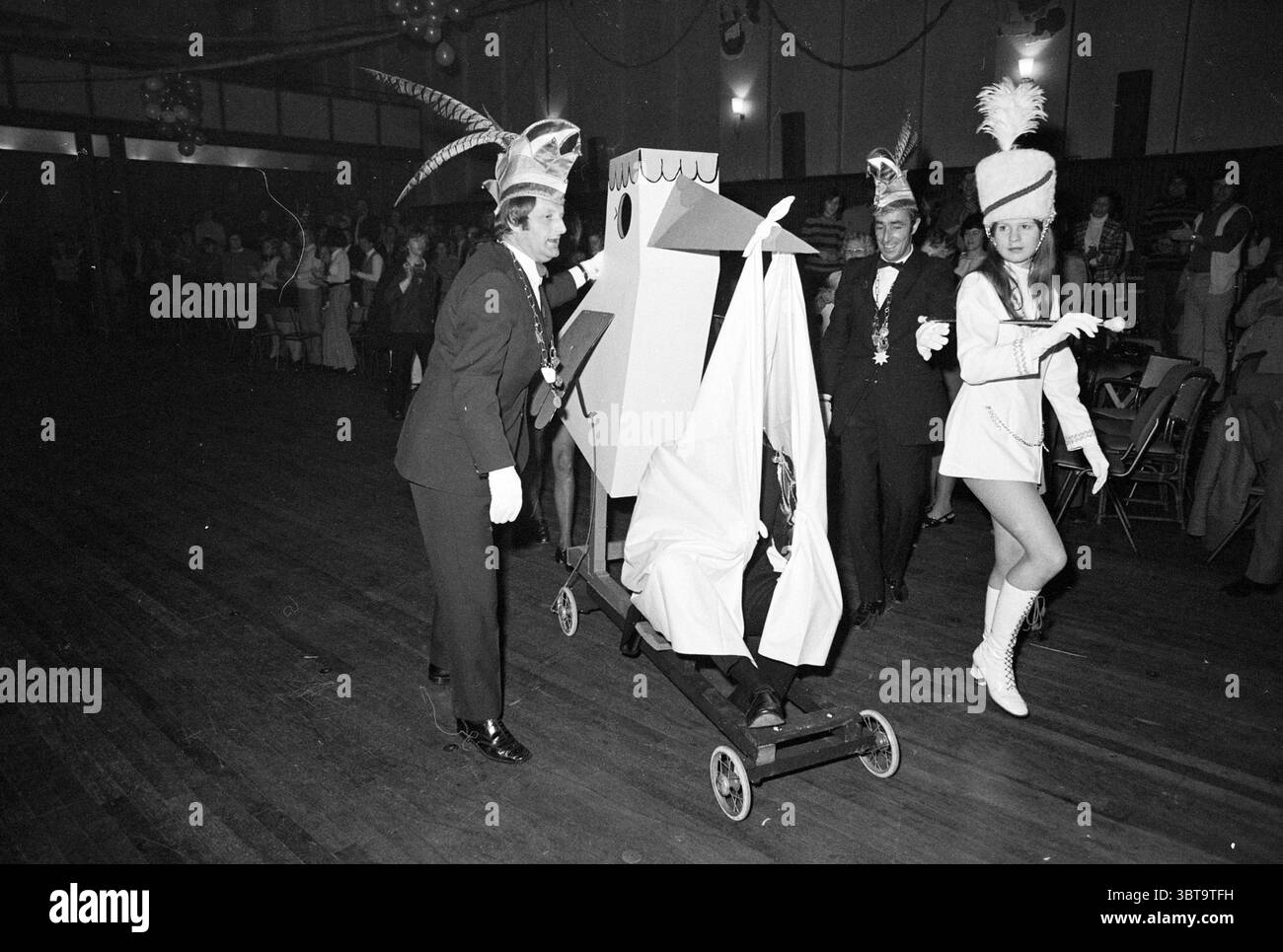 Carnevale Prince Haarlem Carnival, Whizgle News, Dutch Desk, Paesi Bassi, 1950 - 2000 il 08-01-1972. L'immagine mostra questi argomenti. La scena è ambientata in un vivace ambiente interno caratterizzato da un grande spazio aperto con pavimento in legno che riflette l'illuminazione ambientale. L'atmosfera è festosa, arricchita da una folla di persone che amano l'evento. In primo piano, spicca un gruppo di individui vestiti con costumi drammatici che suggeriscono un'occasione celebrativa, magari un carnevale o una festa a tema. A sinistra, una persona in un tubo tiene una struttura simile a un carrello, adornata con sim Foto Stock Carnevale Prince Haarlem Carnival, Whizgle News, Dutch Desk, Paesi Bassi, 1950 - 2000 il 08-01-1972. L'immagine mostra questi argomenti. La scena è ambientata in un vivace ambiente interno caratterizzato da un grande spazio aperto con pavimento in legno che riflette l'illuminazione ambientale. L'atmosfera è festosa, arricchita da una folla di persone che amano l'evento. In primo piano, spicca un gruppo di individui vestiti con costumi drammatici che suggeriscono un'occasione celebrativa, magari un carnevale o una festa a tema. A sinistra, una persona in un tubo tiene una struttura simile a un carrello, adornata con sim Foto Stock