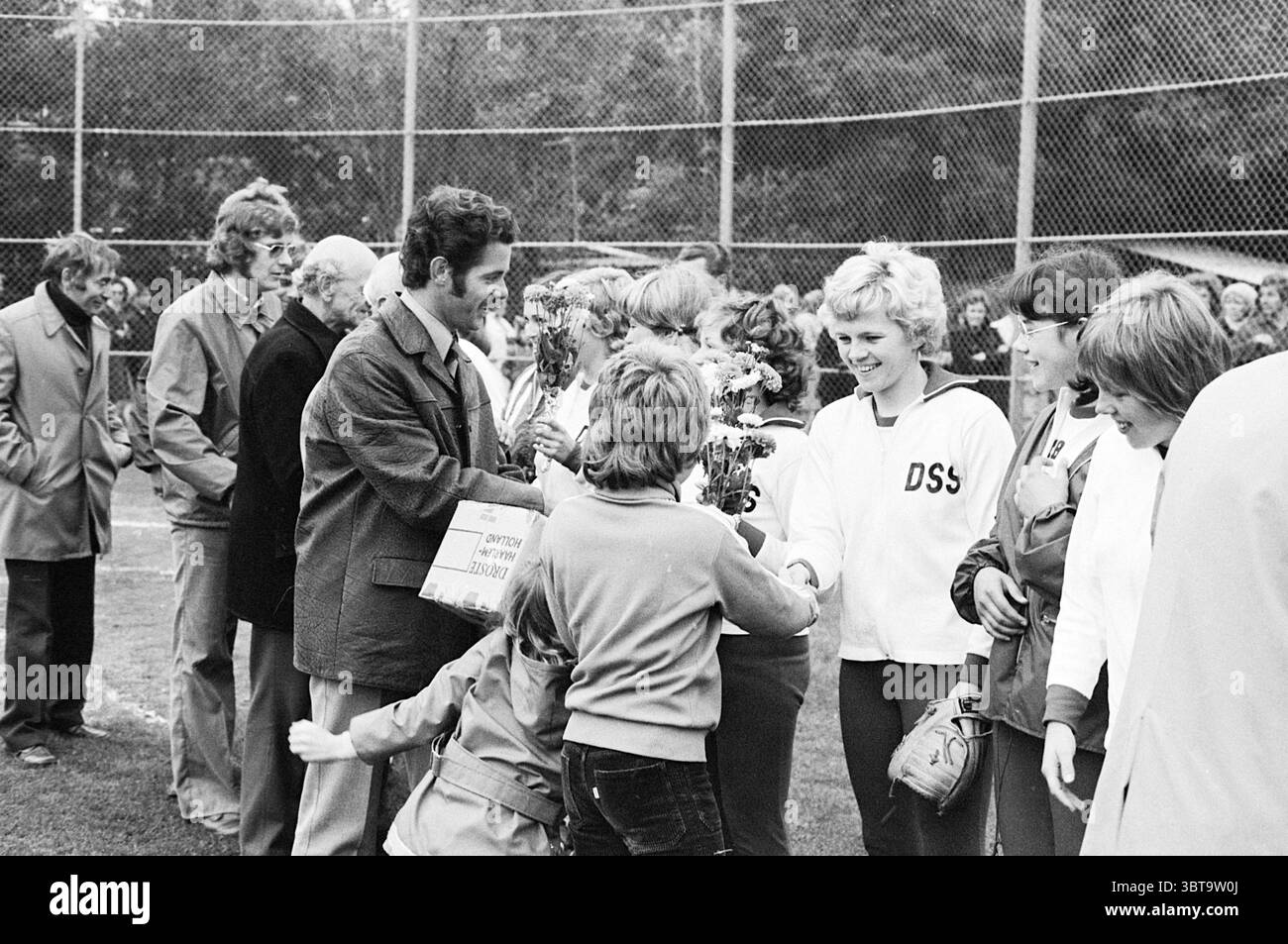 Squadra di softball D.S.S. Copex + squadra H.H.C. tempo squadra + H.H.C. contro D.S.S. Softball, Whizgle News, Dutch Desk, Paesi Bassi, 1950 - 2000 il 21-09-1974. Questi sono gli argomenti nell'immagine. In un ambiente vivace all'aperto, un gruppo di persone è impegnato in un momento di festa o riconoscimento. La scena è adornata di verde, che suggerisce un evento sportivo o comunitario. La luce del sole filtra attraverso gli alberi, creando un'atmosfera calda e invitante, completata da un senso di cameratismo tra i presenti. Le figure centrali includono diversi adulti e bambini, tutti con espressioni gioiose. O Foto Stock