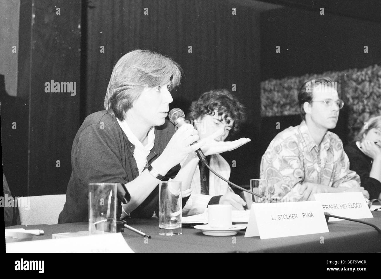 Incontro degli agricoltori nell'Olanda meridionale (Ridderkerk) Ridderkerk, Whizgle News, Dutch Desk, Paesi Bassi, 1950 - 2000 il 30-03-1992. L'immagine contiene questi argomenti. La scena presenta una tavola rotonda ambientata su uno sfondo di pannelli di legno scuro, che trasmettono un'atmosfera professionale. Il tavolo è ricoperto da un panno scuro e vari oggetti, come bicchieri d'acqua e tazze da caffè, sono disposti in modo ordinato prima degli altoparlanti. In primo piano, un individuo con i capelli di media lunghezza tiene un microfono, gestendo con la mano libera, suggerendo che sta facendo un punto importante. Indossano un li Foto Stock