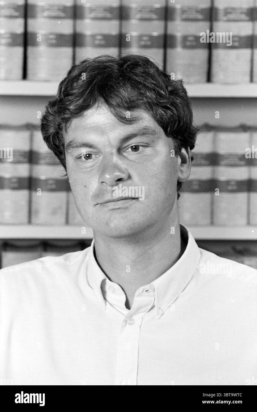 Ritratti di uomini e donne in un ufficio fotografati di fronte a una libreria con libri di legge, Whizgle News, Dutch Desk, Paesi Bassi, 1950 - 2000 nel 1990. Questi argomenti vengono visualizzati nell'immagine. La scena presenta un uomo con capelli scuri leggermente ruvidi, che trasmette un comportamento rilassato ma premuroso. Indossa una camicia button-down di colore chiaro, che contrasta delicatamente con uno sfondo di libri o file disposti in modo ordinato, le loro spine riflettono una gamma di colori tenui, prevalentemente toni terrosi. L'ambientazione sembra essere una biblioteca o un ufficio, fornendo un senso di ricerca intellettuale. L’uomo è stato espulso Foto Stock