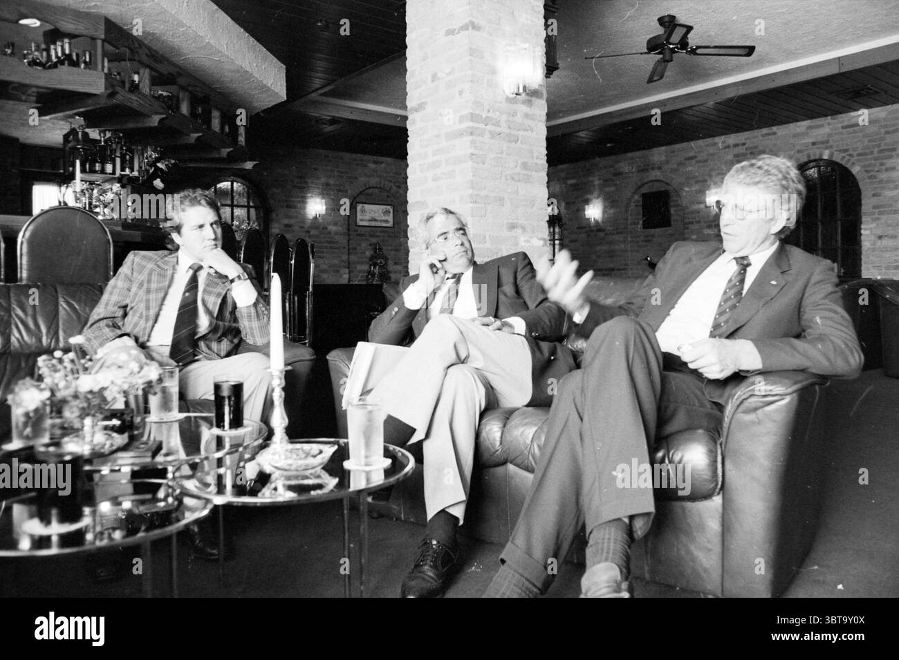 Uomini d'affari che discutono Motel Akersloot persone aziende Akersloot, Whizgle News, Dutch Desk, Paesi Bassi, 1950 - 2000 il 21-05-1986. Questi sono gli elementi dell'immagine. In un ambiente accogliente e poco illuminato, tre uomini si siedono a stretto contatto su un divano in pelle scura e si impegnano in una discussione animata. Ogni individuo ha uno stile distinto, contribuendo all'atmosfera generale della scena. A sinistra, un uomo in un blazer a scacchi con un sottile mix di tonalità grigio e blu appare penoso, potendo il mento sulla sua mano. La sua espressione trasmette un pensiero profondo e i suoi capelli ben curati si completano Foto Stock