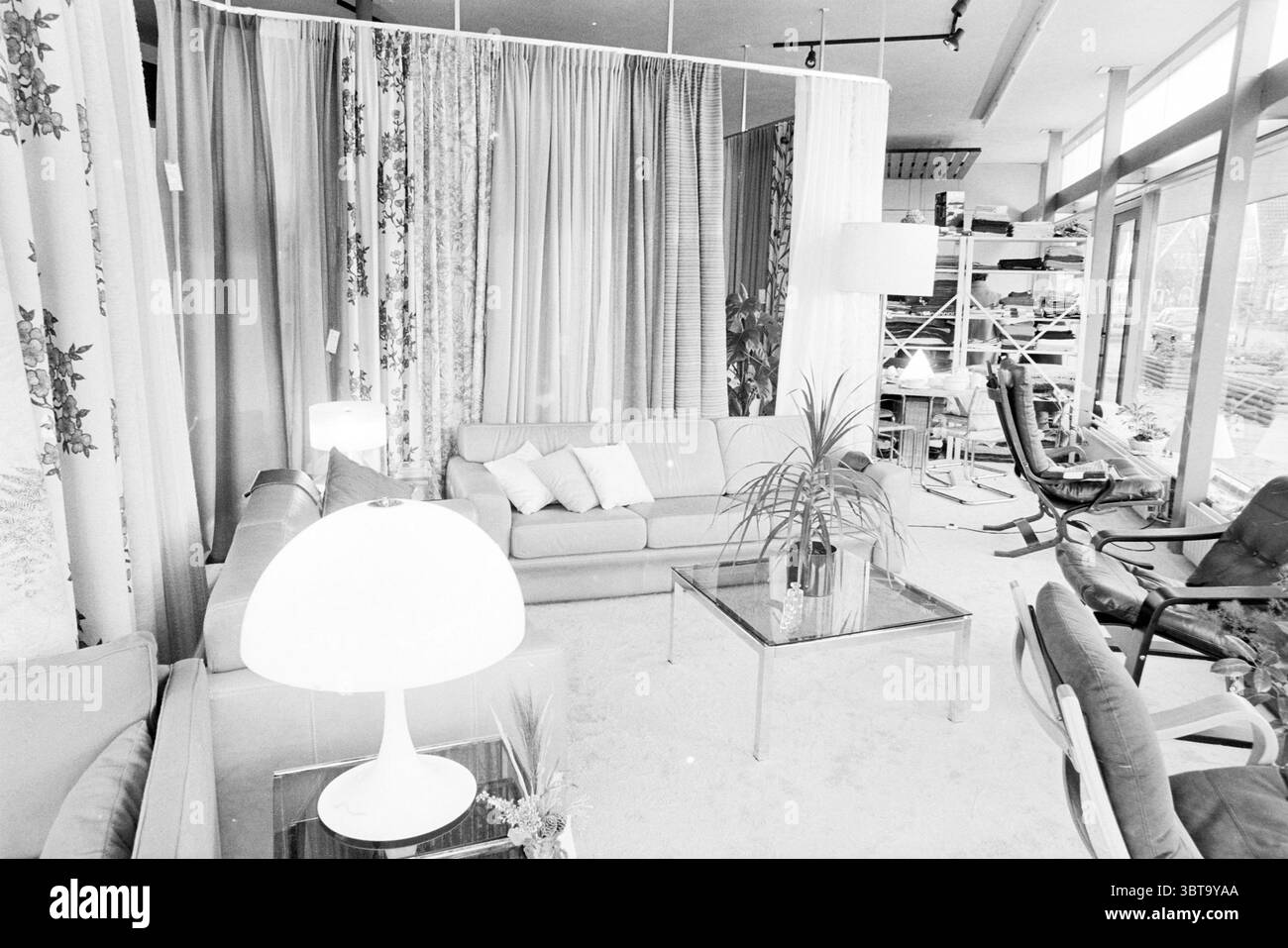 Interni della società Leijsen a Bennebroek negozi d'interni e chioschi Bennebroek, Whizgle News, Dutch Desk, Paesi Bassi, 1950 - 2000 il 03-12-1979. L'immagine contiene questi argomenti. La scena presenta un soggiorno spazioso e moderno caratterizzato dal suo design elegante e dall'estetica minimalista. L'illuminazione soffusa inonda l'area, creando un'atmosfera calda e invitante nonostante le tonalità monocromatiche. In primo piano, un morbido divano a L domina la disposizione dei posti a sedere, rivestito in un tessuto leggero. È dotato di diversi cuscinetti rettangolari che offrono un tocco di comfort e contrasto. Adiacente Foto Stock