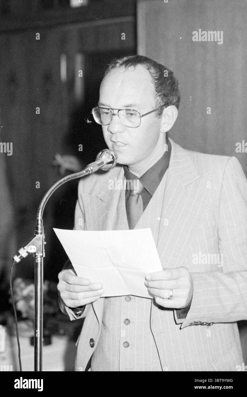 Ricevimento di addio, signor Cutter. VNU Association of Dutch Publishers, Whizgle News, Dutch Desk, Paesi Bassi, 1950 - 2000 il 06-10-1978. Questi sono gli argomenti nell'immagine. La scena vede un uomo in piedi davanti a un microfono, impegnato in un discorso o una presentazione. È vestito con un abito elegante e con pinstrime, che conferisce un'atmosfera formale e retrò all'ambiente. La tuta è composta da strisce di colore chiaro su un tessuto più scuro, che ne esaltano l'aspetto professionale. I suoi occhiali gli incorniciano il viso, aggiungendo un tocco intellettuale, mentre tiene un pezzo di carta in una mano, probabilmente facendo riferimento alle sue note. T Foto Stock