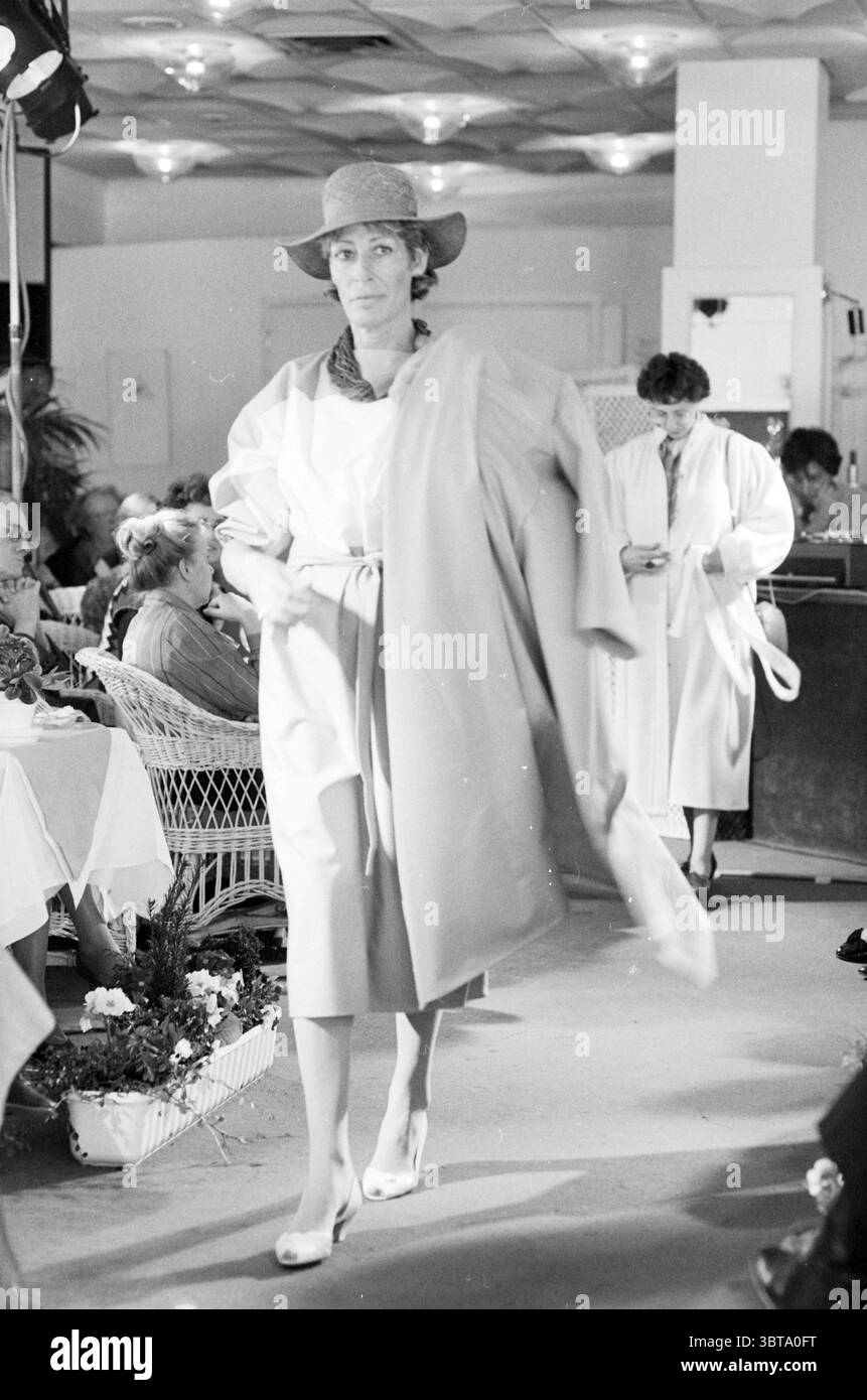 Hotel per sfilate di moda Bouwes Zandvoort Fashion Zandvoort, Whizgle News, Dutch Desk, Paesi Bassi, 1950 - 2000 il 21-03-1986. Questi argomenti sono mostrati nell'immagine. La scena cattura un momento di passerella elegante all'interno di un sofisticato ambiente interno, caratterizzato da un'illuminazione soffusa che diffonde una calda luce soffusa in tutto lo spazio. In primo piano, un modello si muove con sicurezza lungo un passaggio leggermente rialzato, mostrando un abbigliamento elegante. L'ensemble presenta linee fluide, con un delicato tono pastello che si armonizza con la gamma di colori delicati della scena. Indossa un cappello a tesa larga Foto Stock