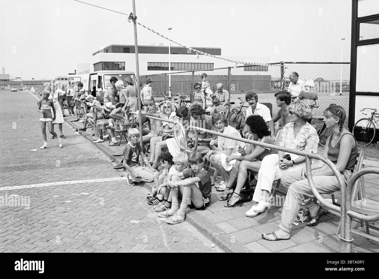 Mosquito Round Mosquito Round 28-07-1980, 29-07-1980, 31-07-1980, 01-08-1980, Whizgle News, Dutch Desk, Paesi Bassi, 1950 - 2000 il 02-08-1980. L'immagine mostra questi argomenti. In un vivace ambiente all'aperto, un grande gruppo di persone siede lungo una lunga e bassa panchina che si estende in primo piano. La folla sembra essere un mix di adulti e bambini di varie età, ognuno impegnato in conversazione o in silenzio osservando l'ambiente circostante. Alcuni individui si inclinano in avanti, animati nella discussione, mentre altri sembrano più rilassati, godendosi il sole. La tavolozza dei colori è prevalentemente mon Foto Stock