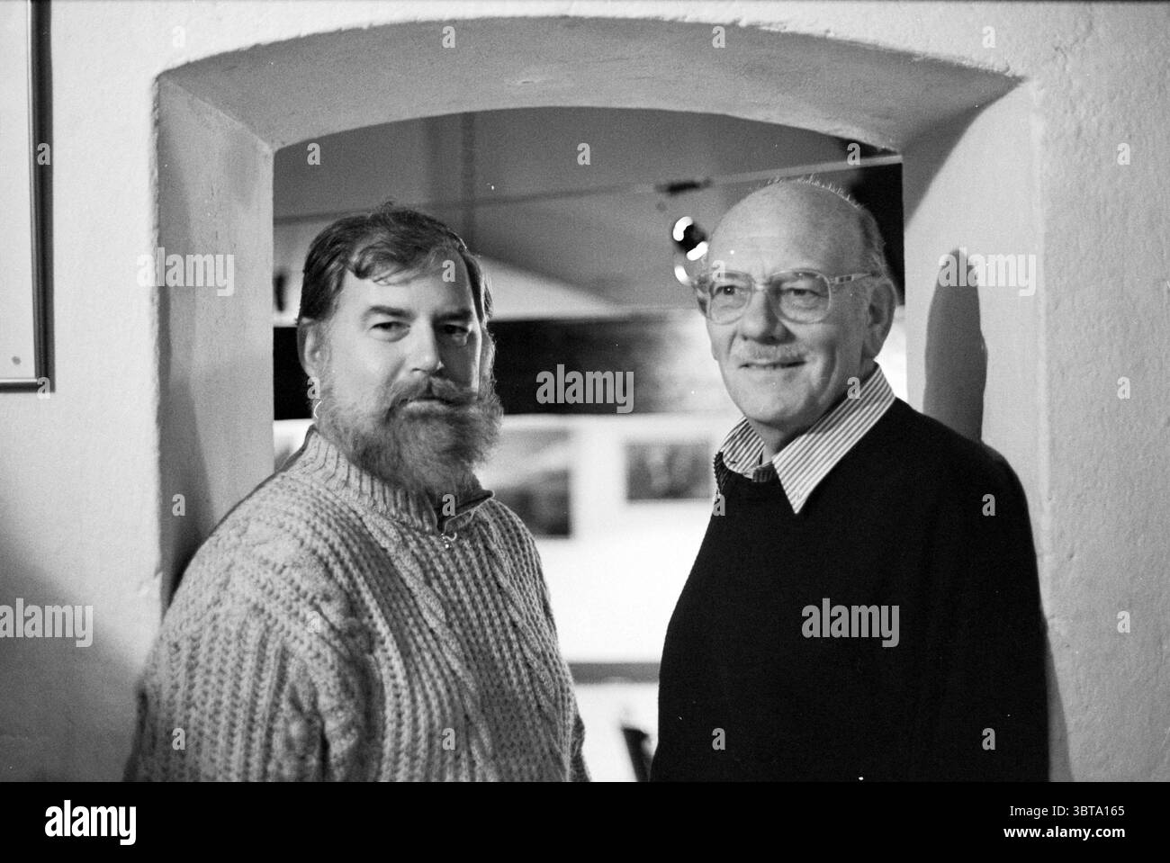 Ritratto due uomini, Whizgle News, Dutch Desk, Paesi Bassi, 1950 - 2000 il 02-11-1993. L'immagine include questi argomenti. Due uomini si trovano fianco a fianco all'interno di un'alcova illuminata con un arco arrotondato. L'ambiente trasuda un'atmosfera calda e accogliente, impreziosita da ombre sottili create dall'illuminazione sopra. L'uomo sulla sinistra ha una barba spessa e ben curata e indossa un comodo maglione a filo dai colori chiari. La sua espressione è premurosa, suggerisce profondità e saggezza, con le braccia rilassate ai lati. La consistenza del suo maglione contrasta delicatamente con le superfici più lisce intorno a lui. A. Foto Stock