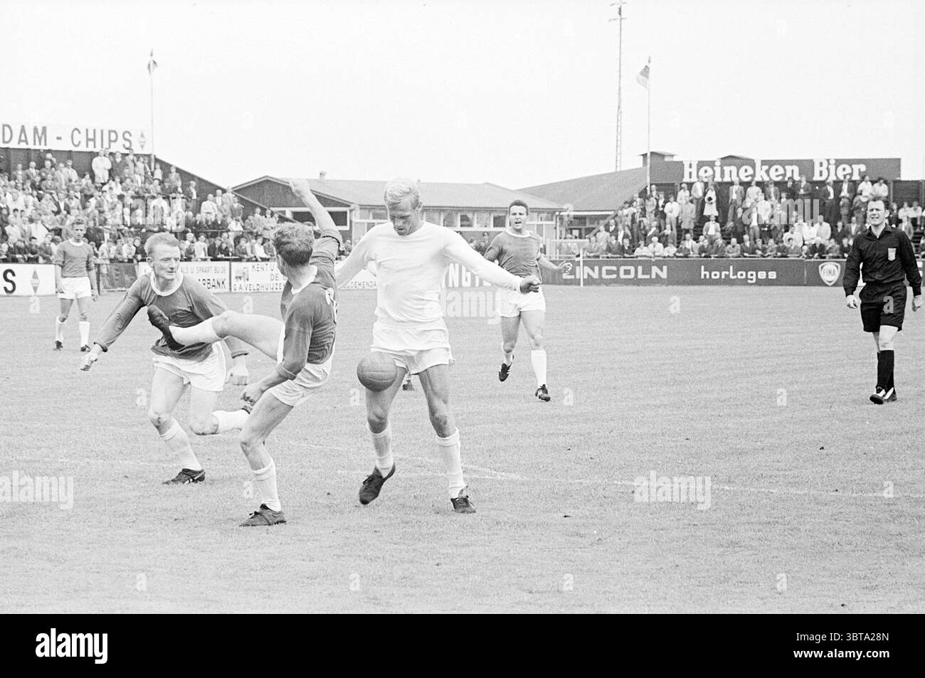 RCH - Telstar Football R.C.H., Whizgle News, Dutch Desk, Paesi Bassi, 1950 - 2000 il 30-07-1967. Questi argomenti sono mostrati nell'immagine. La scena cattura un momento intenso su un campo da calcio erboso, illuminato da una luce soffusa e naturale che suggerisce una giornata travolgente. In primo piano, due giocatori di squadre avversarie sono impegnati in un gioco dinamico; un giocatore, vestito con un abbigliamento di colore chiaro, controlla abilmente la palla mentre tenta di manovrare intorno al suo avversario, che è in una marcia più scura e sembra essere in procinto di essere un tackle difensivo. I giocatori esibiscono espressioni mirate, Foto Stock