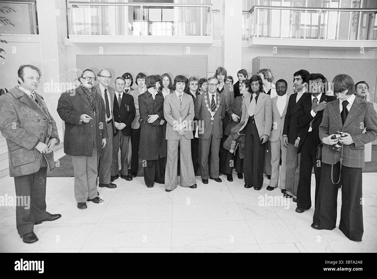 Il sindaco Reehorst riceve i ricevimenti dei sindaci Velsen, Whizgle News, Dutch Desk, Paesi Bassi, 1950 - 2000 il 23-03-1976. Questi sono gli elementi dell'immagine. La scena cattura un gruppo diversificato di individui riuniti all'interno, probabilmente in una lobby o atrio spazioso e ben illuminato caratterizzato da elementi architettonici moderni. L'ambiente ha un aspetto pulito e lucido, con pavimento in marmo liscio e illuminazione luminosa e ariosa che crea un ambiente professionale. Le persone presenti mostrano una gamma di abbigliamento, prevalentemente formale e semi-formale tipico degli anni '1970 Molti usurano S. Foto Stock