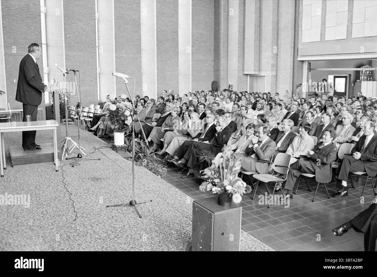 25° anniversario del Pio X College Beverwijk (relatore e pubblico ridendo in auditorium), Whizgle News, Dutch Desk, Paesi Bassi, 1950 - 2000 il 15-09-1979. L'immagine contiene questi argomenti. La scena è ambientata in uno spazioso auditorium interno, caratterizzato da alti soffitti e grandi pareti adornate da semplici linee verticali di mattoni. L'umore trasmette un senso di formalità e attenzione, poiché numerose persone sono sedute in fila, di fronte a un punto focale centrale. Il pubblico è prevalentemente vestito con abiti formali, con uomini in abiti e donne in abiti, che riflettono un senso di occasione. fanno schifo Foto Stock