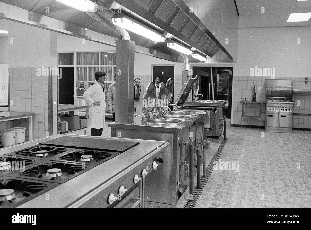 Cucina interna Scuola di cucina Ripperdakazerne Haarlem Paesi Bassi, Whizgle News, Dutch Desk, Paesi Bassi, 1950 - 2000 il 06-02-1979. Questi sono gli elementi dell'immagine. La scena presenta un'ampia disposizione industriale della cucina, con particolare attenzione alla funzionalità e all'efficienza. Gli elettrodomestici in acciaio inox dominano lo spazio, riflettendo una lucentezza lucida sotto una luminosa illuminazione superiore. A sinistra è visibile una serie di bruciatori a gas, ciascuno con comandi disposti meticolosamente, che indicano vari livelli di calore. Accanto alle stufe, grandi vasi rotondi sono arroccati in cima, con le loro superfici lucide Foto Stock