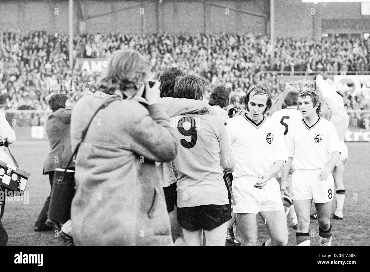 Paesi Bassi - Belgio calcio Paesi Bassi, Whizgle News, Dutch Desk, Paesi Bassi, 1950 - 2000 il 18-11-1973. Questi sono gli elementi dell'immagine. La scena cattura un vivace evento sportivo, pieno di emozioni ed emozioni. Al centro, un gruppo di atleti che indossano uniformi abbinate si riunisce in un abbraccio celebrativo, le loro espressioni irradiano gioia e cameratismo. Un atleta, che indossa il numero “9”, si erge in modo prominente, impegnato nel momento con i compagni di squadra intorno a lui. Sullo sfondo, una grande folla di spettatori riempie gli stand, i loro volti mostrano varie reazioni, dall'euforia al Foto Stock