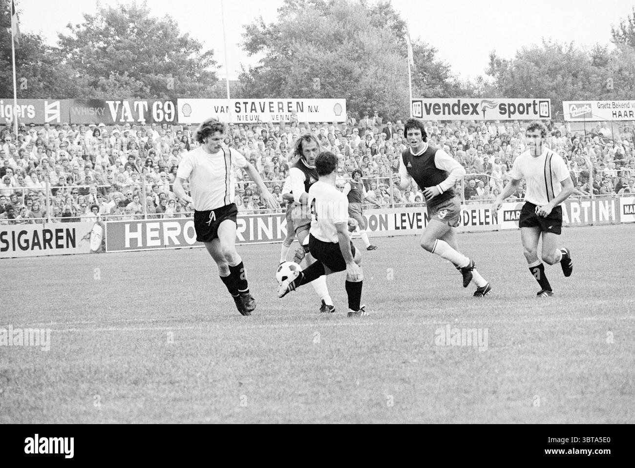 Haarlem - NAC Football Haarlem, Whizgle News, Dutch Desk, Paesi Bassi, 1950 - 2000 il 19-08-1973. L'immagine include questi argomenti. La scena cattura un momento dinamico su un campo da calcio erboso, dove l'emozione riempie l'aria. In primo piano, un giocatore con una maglia a strisce bianche e nere manovra abilmente la palla, mostrando agilità e concentrazione. La sua postura suggerisce concentrazione, mentre si prepara a fare un gioco decisivo. Intorno a lui ci sono diversi concorrenti, ognuno con divise distinte: Uno in un gilet nero, l'altro in una camicia bianca e l'ultimo in un vestito nero. I loro expres Foto Stock