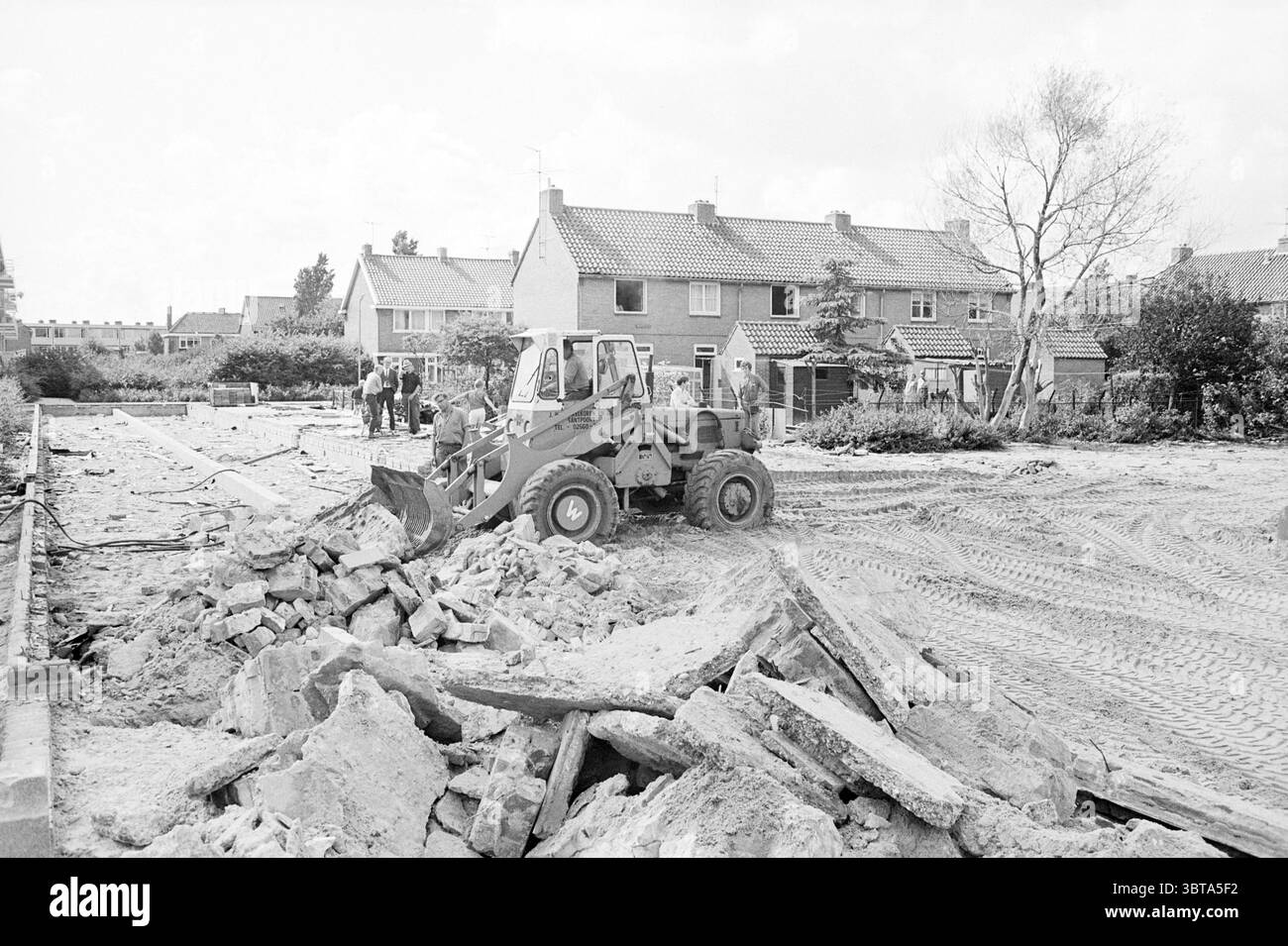 Demolizione delle scuole scolastiche, Whizgle News, Dutch Desk, Paesi Bassi, 1950 - 2000 il 20-08-1969. L'immagine include questi argomenti. La scenografia cattura un'area di costruzione in fase di cambiamento significativo. Al centro del primo piano c'è un bulldozer giallo e grigio con una benna a caricamento frontale, adagiata su un terreno irregolare cosparso di macerie e detriti. Frammenti di calcestruzzo e pietra sono sparsi intorno, a indicare lavori di demolizione o scavo in corso. Sullo sfondo si può vedere una fila di case modeste con tetti inclinati, ognuna con una varietà di colori tenui come beige chiaro e blu pallido, BL Foto Stock