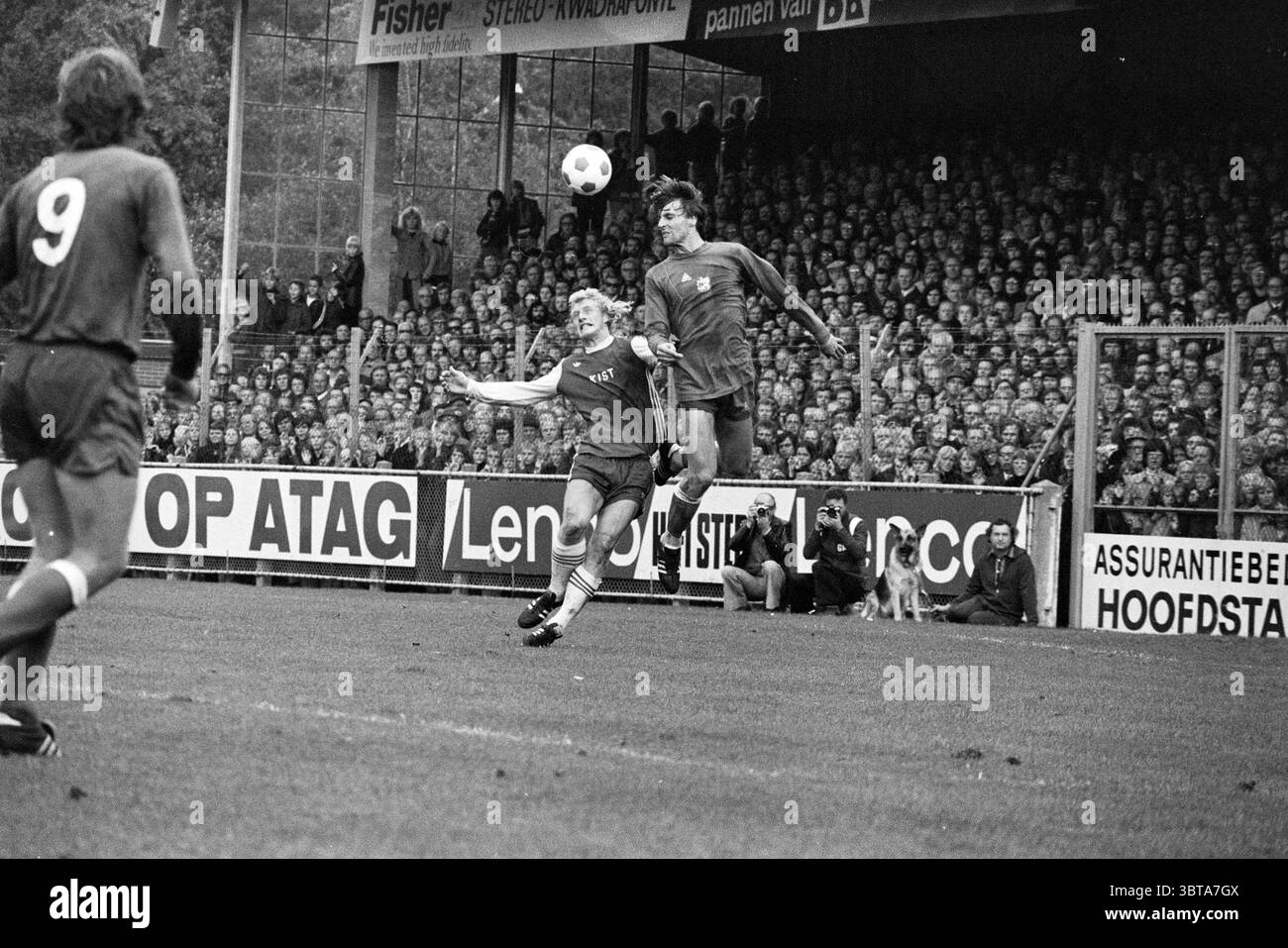 AZ'67 - Ajax Football Ajax, Whizgle News, Dutch Desk, Paesi Bassi, 1950 - 2000 il 05-10-1975. Questi argomenti sono mostrati nell'immagine. Sulla scena, una partita di calcio dinamica si svolge su un campo in erba ben tenuto. L'attenzione è rivolta a due giocatori: Uno è a mezz'aria, saltando per entrare in contatto con un pallone da calcio volante, mentre l'altro è pronto a difendersi o intercettare. Entrambi gli atleti sono vestiti con uniformi abbinate, una con sfumature più profonde e l'altra con un tono più chiaro, creando un contrasto che attira l'attenzione. Lo sfondo è pieno di una folla densa, i loro volti sono un mix di eccitazione e anticipazione. Foto Stock