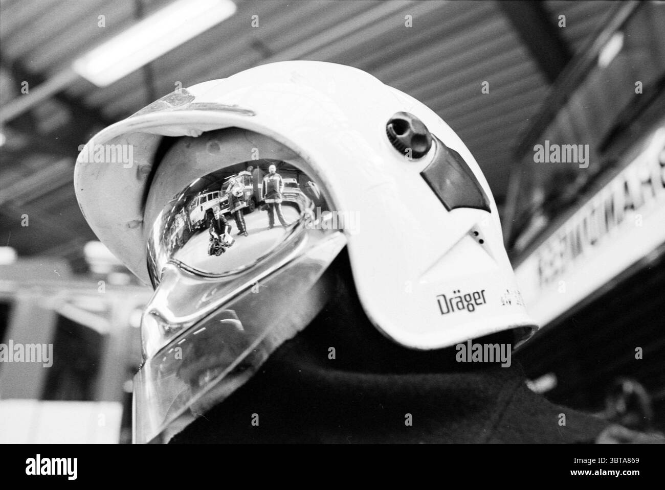 Casco antincendio Dräger, Whizgle News, Dutch Desk, Paesi Bassi, 1950 - 2000 il 12-04-1995. L'immagine include questi argomenti. La scena cattura una vista ravvicinata di un casco, prevalentemente bianco e dotato di visiera trasparente. La superficie lucida del casco riflette varie figure ed elementi dell'ambiente circostante. Nella riflessione, sono visibili le sagome delle persone, alcune delle quali sembrano coinvolte in conversazioni o attività orientate alle attività. La presenza di attrezzature antincendio o veicoli nelle vicinanze suggerisce un'impostazione di risposta alle emergenze, suscitando un senso di urgenza e concentrazione. La tavolozza dei colori è quasi Foto Stock