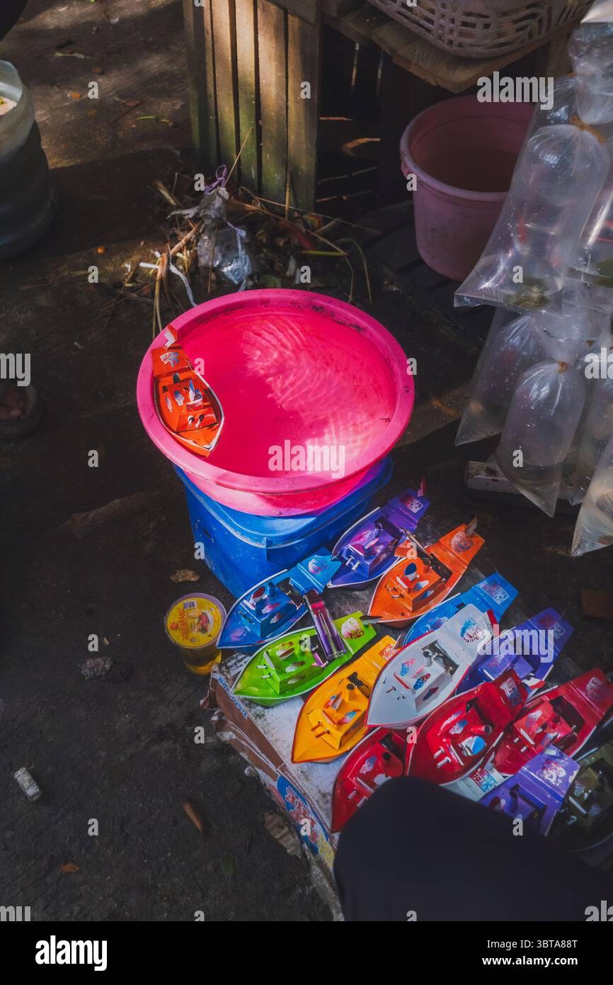 Balikpapan, Indonesia - 19 aprile 2025. Assortimento di barche giocattolo colorate disposte vicino a un secchio d'acqua al mercato Pandan Sari, catturando nostalgici Foto Stock