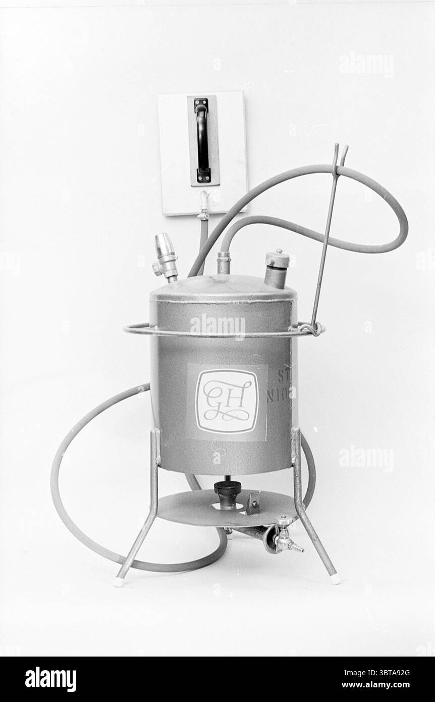 Parti e pacchetti Goudsmit Hof. Goudsmit - Hof, Whizgle News, Dutch Desk, Paesi Bassi, 1950 - 2000 il 30-11-1965. Questi argomenti sono mostrati nell'immagine. La scena presenta un contenitore in metallo dal design complesso, che si erge in posizione verticale su una struttura robusta e minimalista. Questa tanica è dipinta in una tonalità di grigio profonda, completata da una sottile lucentezza che riflette la luce ambientale. Un logo prominente, eventualmente un emblema o delle iniziali, è visibile sul lato in un colore a contrasto, conferendo carattere all'oggetto. Collegato al contenitore è presente un tubo lungo e flessibile, che si avvolge agevolmente prima di estendere l'outwa Foto Stock