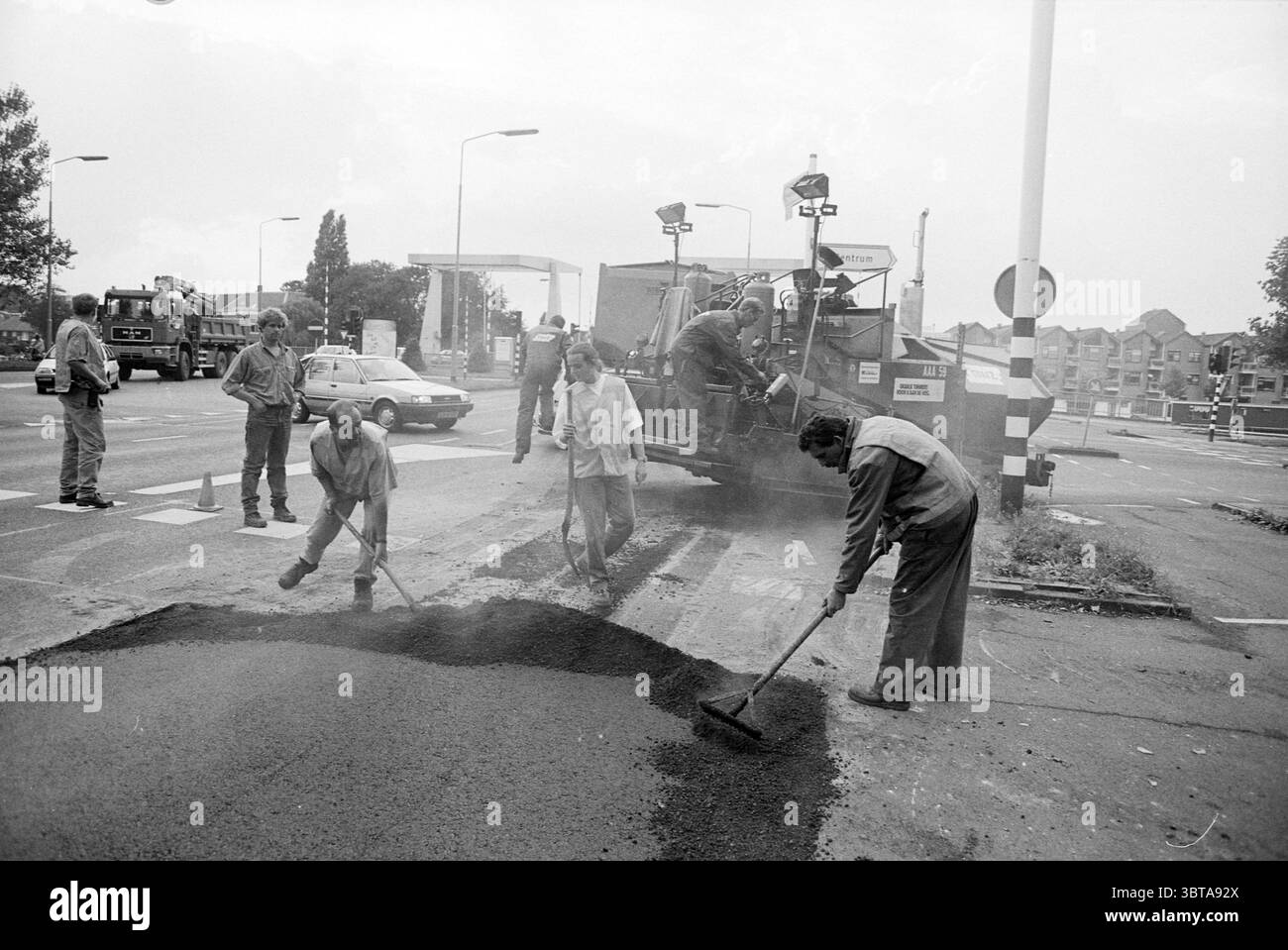 Asperting Schipholweg Schipholweg, Whizgle News, Dutch Desk, Paesi Bassi, 1950 - 2000 il 11-09-1995. L'immagine include questi argomenti. La scena raffigura una vivace area urbana di lavoro stradale, caratterizzata da un mix di attività e macchinari. In primo piano, diversi lavoratori sono fortemente impegnati nell'attività di applicazione dell'asfalto. Indossano abiti casual e resistenti alle intemperie, che sembrano concentrati e laboriosi. Alcuni sono piegati, spalano asfalto scuro e ruvido, mentre altri si trovano nelle vicinanze, magari dirigendo il posizionamento o gestendo i materiali. Lo sfondo mostra una macchina grande e imponente che Foto Stock