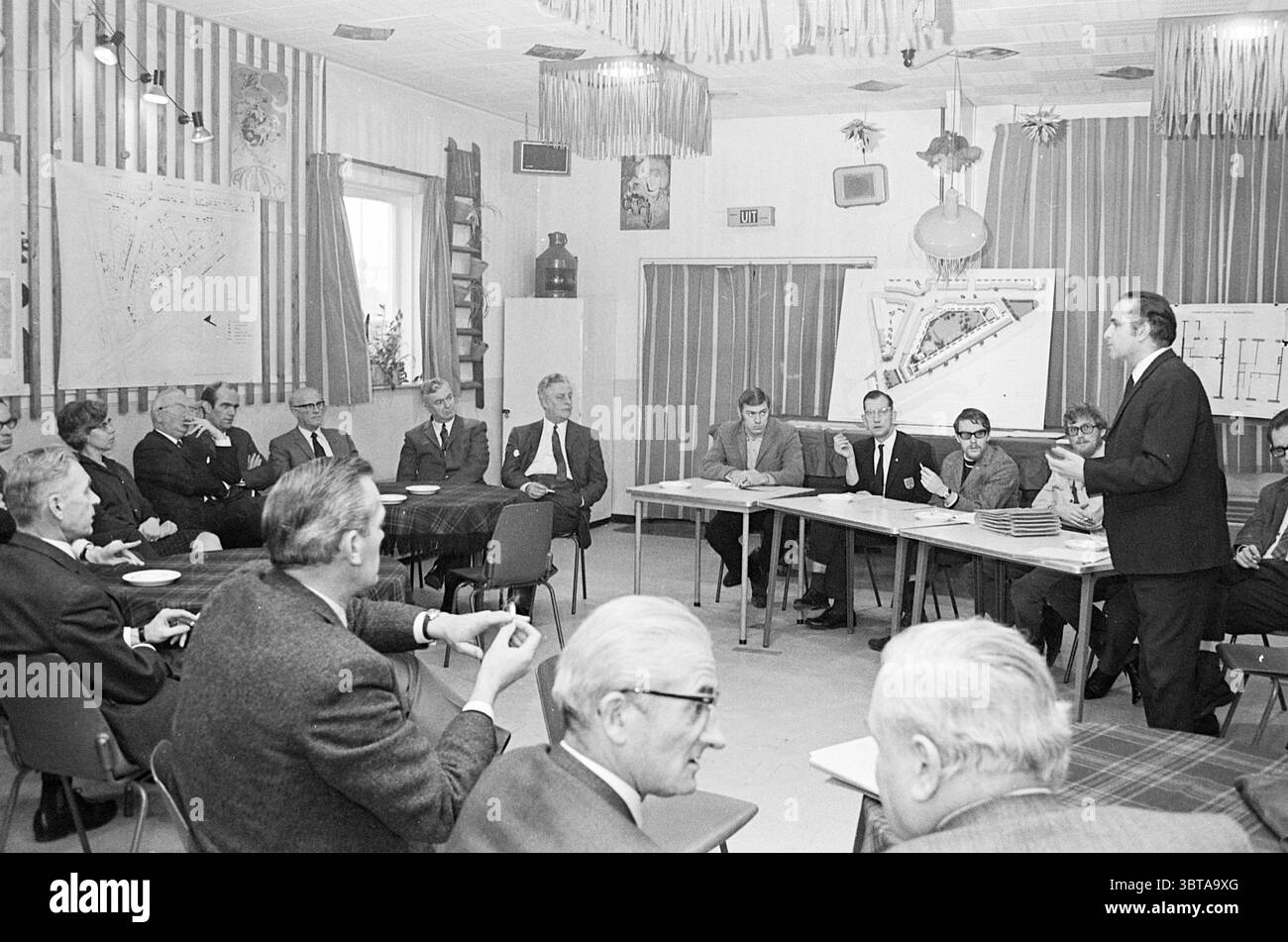 Riunioni del comitato per gli alloggi, Whizgle News, Dutch Desk, Paesi Bassi, 1950 - 2000 il 30-01-1970. Questi sono gli elementi dell'immagine. In una camera spaziosa con un'atmosfera rilassata ma formale, diverse file di persone sono sedute, prevalentemente uomini più anziani. Sono impegnati in una discussione, con alcuni che appaiono attenti, mentre altri sono profondamente pensati. Gli individui sono vestiti con abiti classici, come abiti e cravatte, che aggiungono al tono serio del raduno. L'ambientazione presenta un mix di colori pastello chiari sulle pareti e sono presenti tende verticali a righe che suggeriscono un aes vintage Foto Stock