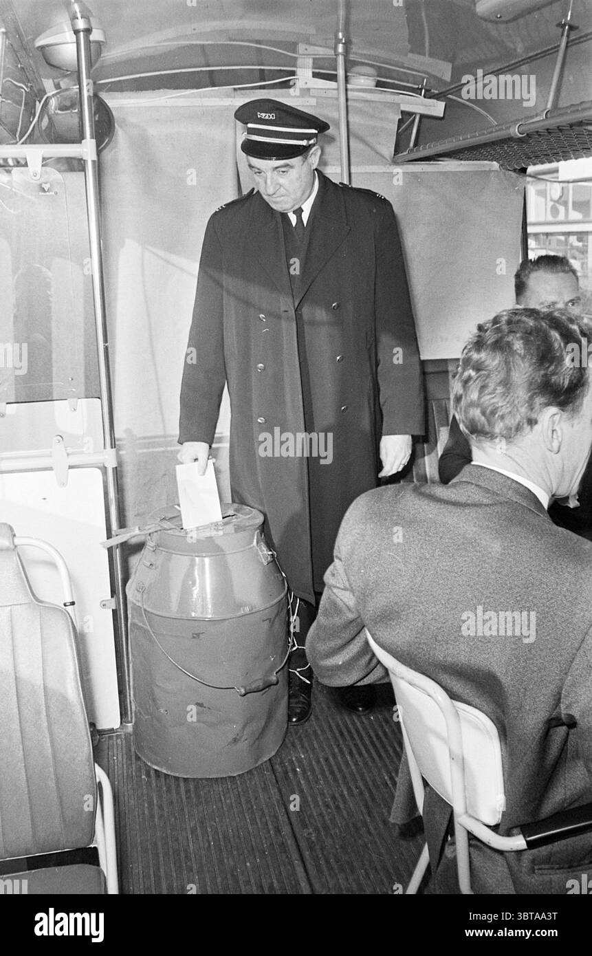 Voti del comitato aziendale Noord Zuid Hollandse Vervoersmaatschappij N.V. NZ, Whizgle News, Dutch Desk, Paesi Bassi, 1950 - 2000 il 26-11-1970. L'immagine contiene questi argomenti. In un abitacolo scarsamente illuminato, la scena si sviluppa all'interno di un veicolo di trasporto pubblico, probabilmente un autobus. L'attenzione è rivolta a una figura vestita con una classica uniforme, completa di cappotto scuro e cappellino, che trasuda un'aria di autorità. Questo individuo si erge accanto ad un contenitore cilindrico che sembra essere una scatola di palline, caratterizzata dal suo colore rosso brillante, che aggiunge un tocco di colore contrastante alle tonalità più attenuate dell'ambiente circostante. A. Foto Stock
