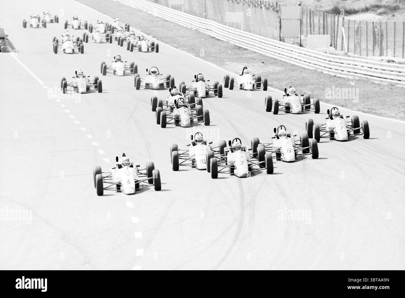 Gara automobilistica Zandvoort Zandvoort, Whizgle News, Dutch Desk, Paesi Bassi, 1950 - 2000 il 19-04-1992. Questi sono gli elementi dell'immagine. La scena cattura un momento dinamico su un circuito, con una serie di auto da corsa allineate in una formazione stretta. I veicoli, principalmente piccoli veicoli a ruota aperta, sono prevalentemente verniciati in varie tonalità di bianco e grigio chiaro, creando un aspetto uniforme ma sorprendente. Le vetture sono dotate di etichette numeriche distinte sui lati, che indicano i singoli concorrenti. L'impostazione è una pista per asfalto, fiancheggiata da una barriera bianca allineata in modo ordinato Foto Stock