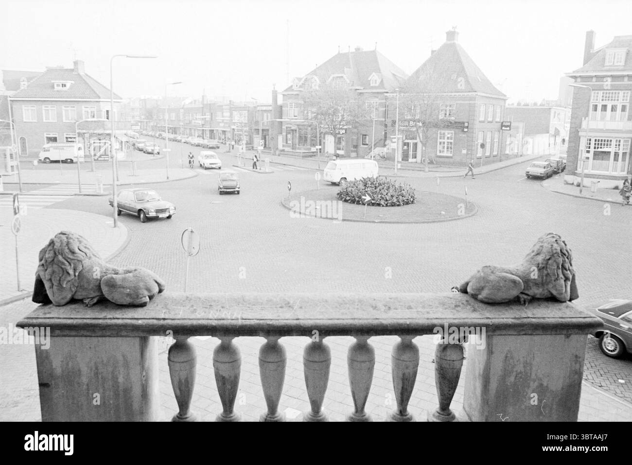 Panoramica Gasthuisplein + Raadhuisplein Zandvoort Zandvoort Gasthuisplein, Whizgle News, Dutch Desk, Paesi Bassi, 1950 - 2000 il 12-10-1978. Questi argomenti vengono visualizzati nell'immagine. La scena presenta un'intersezione circolare, catturata in una tavolozza monocromatica che evoca un senso di nostalgia. In prima linea, due statue di leoni arroccate su una balaustra conferiscono un tocco di grandezza, le loro superfici testurizzate accentuate dalla luce soffusa. La strada è costeggiata da un mix di edifici residenziali e commerciali, che mostrano vari stili architettonici. Le strutture sono prevalentemente solide e rettangolari Foto Stock